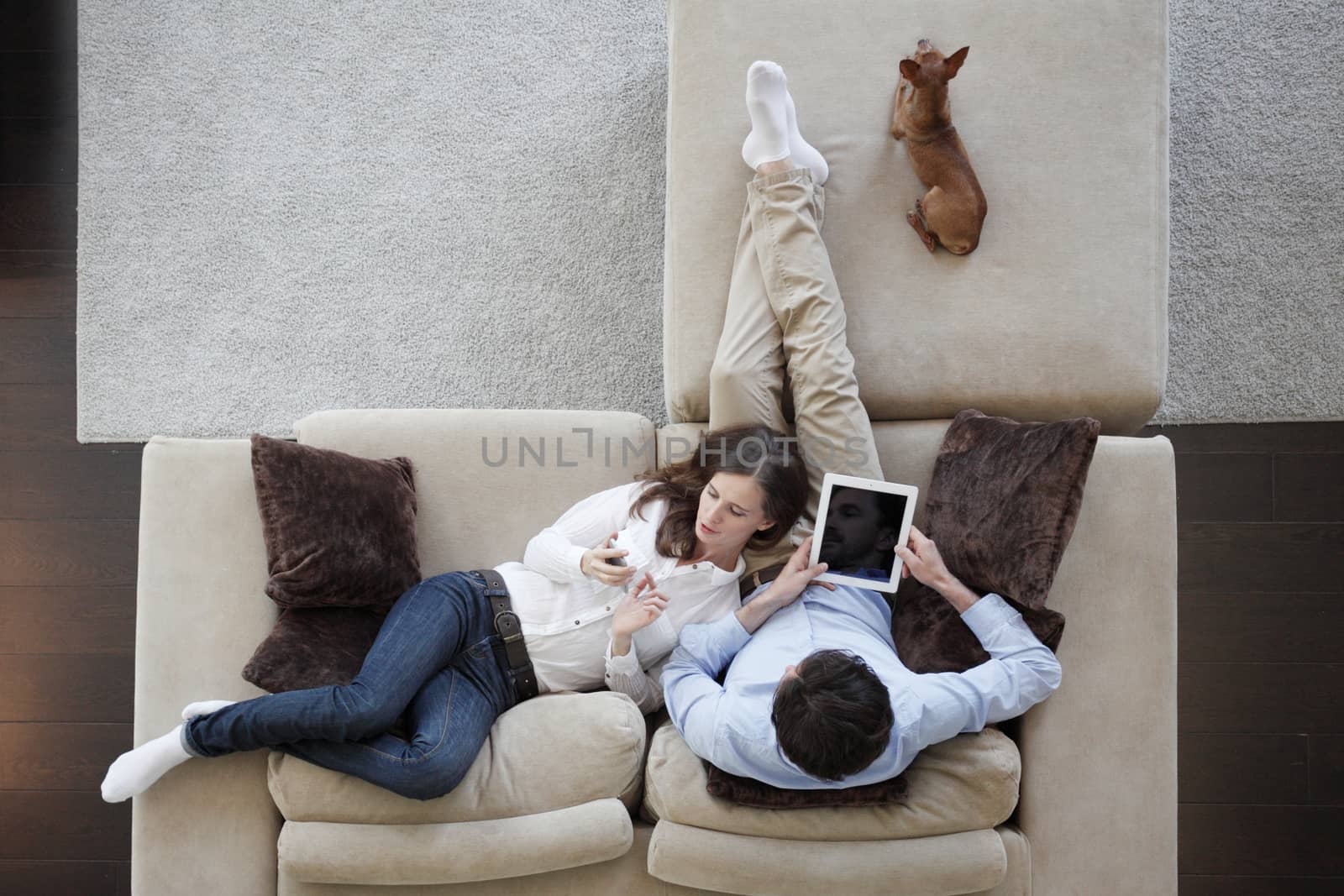 Couple using digital tablet at home sitting on sofa, top view