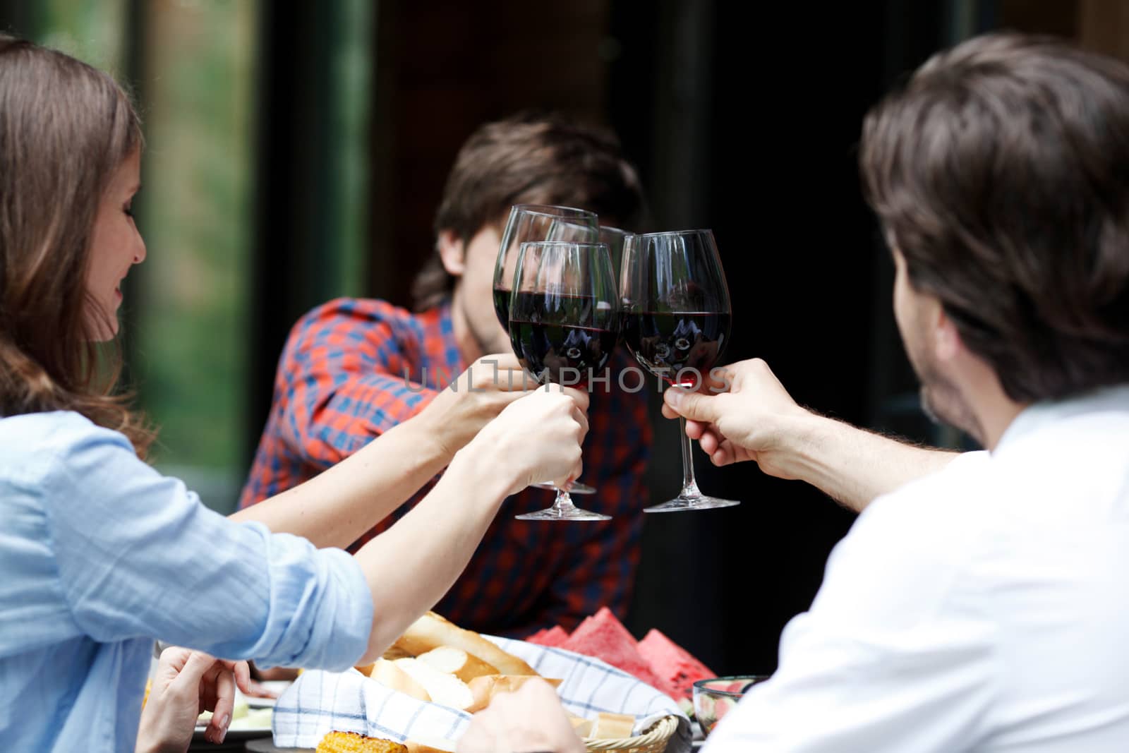 Friends clink glasses of red wine at outdoor dinner