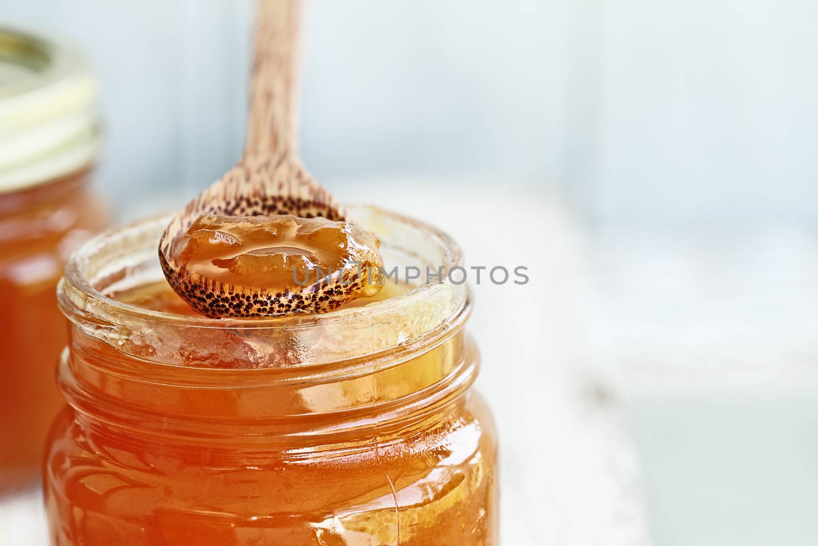 Front View of the tip of a wooden spoon full of homemade Cantaloupe Jam resting on an open jar filled with jam. Extreme shallow depth of field with selective focus on spoonful of preserves. Image could also be used for peach jelly or a marmalde. 