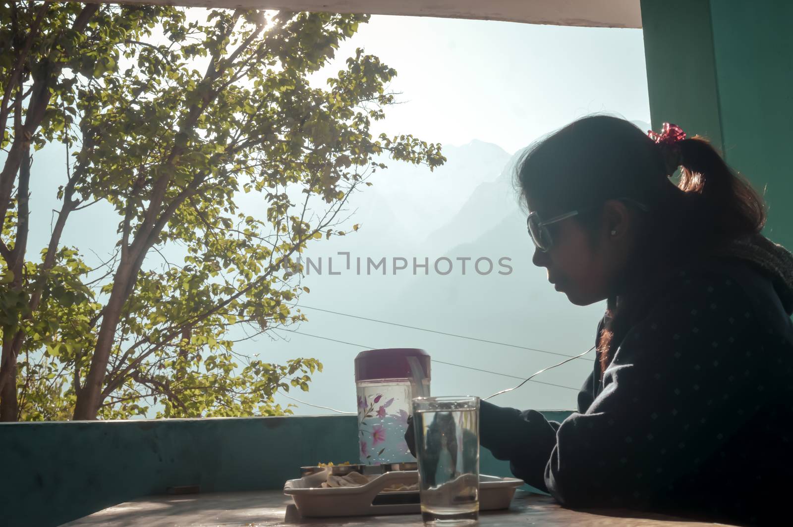 Woman having food taking breakfast while sitting on a dining table in morning at holiday home against Himalayas mountains background. by sudiptabhowmick