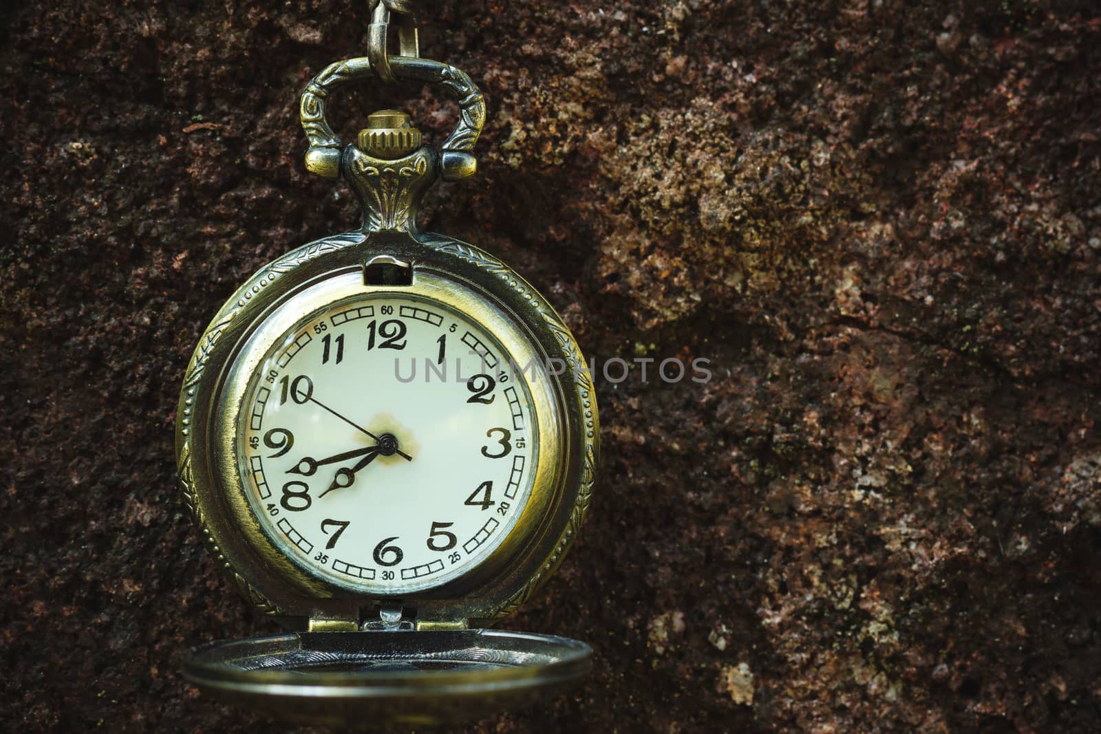 Vintage old pocket watch hanged on the rock background. by SaitanSainam