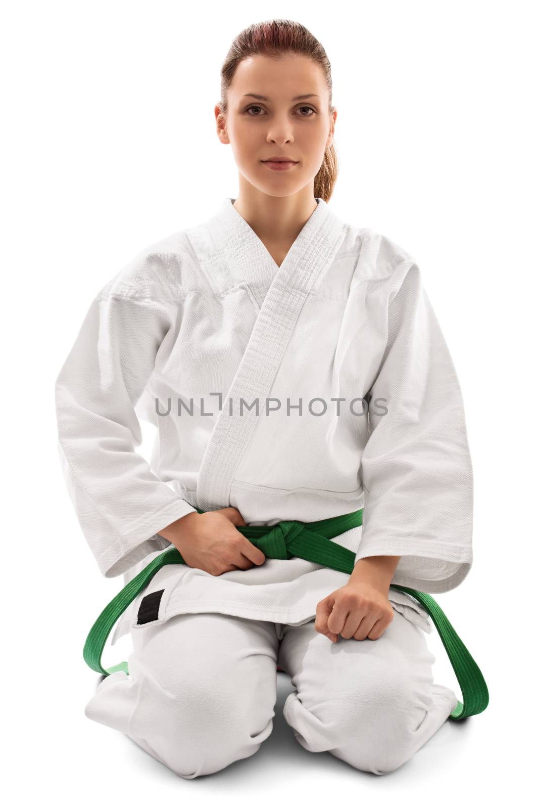 Portrait of a beautiful female martial arts fighter in a white kimono with green belt in the seiza position, isolated on white background. Calm young girl in a kimono kneeling down.