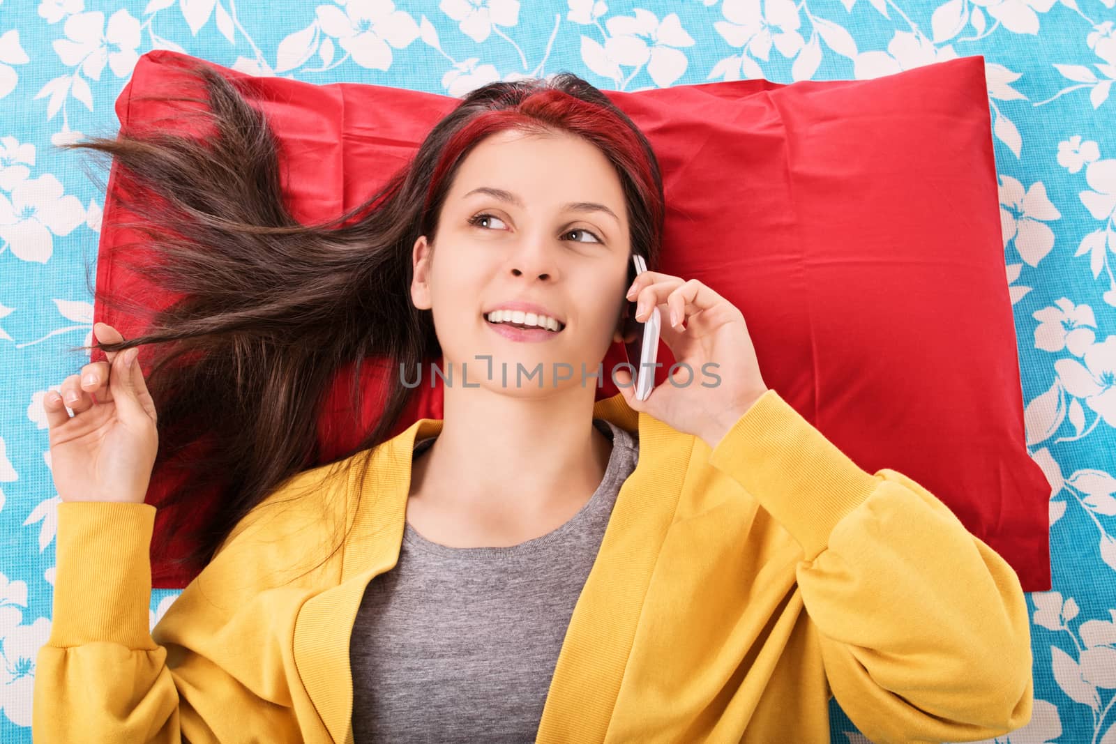 Communication, friendship concept. Beautiful young woman lying in bed, playing with her hair and talking on the mobile phone. Young girl in bed smiling and talking on the phone.