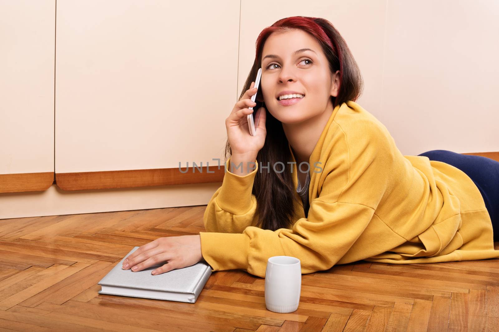 Young woman lying on the floor and talking on the phone by Mendelex