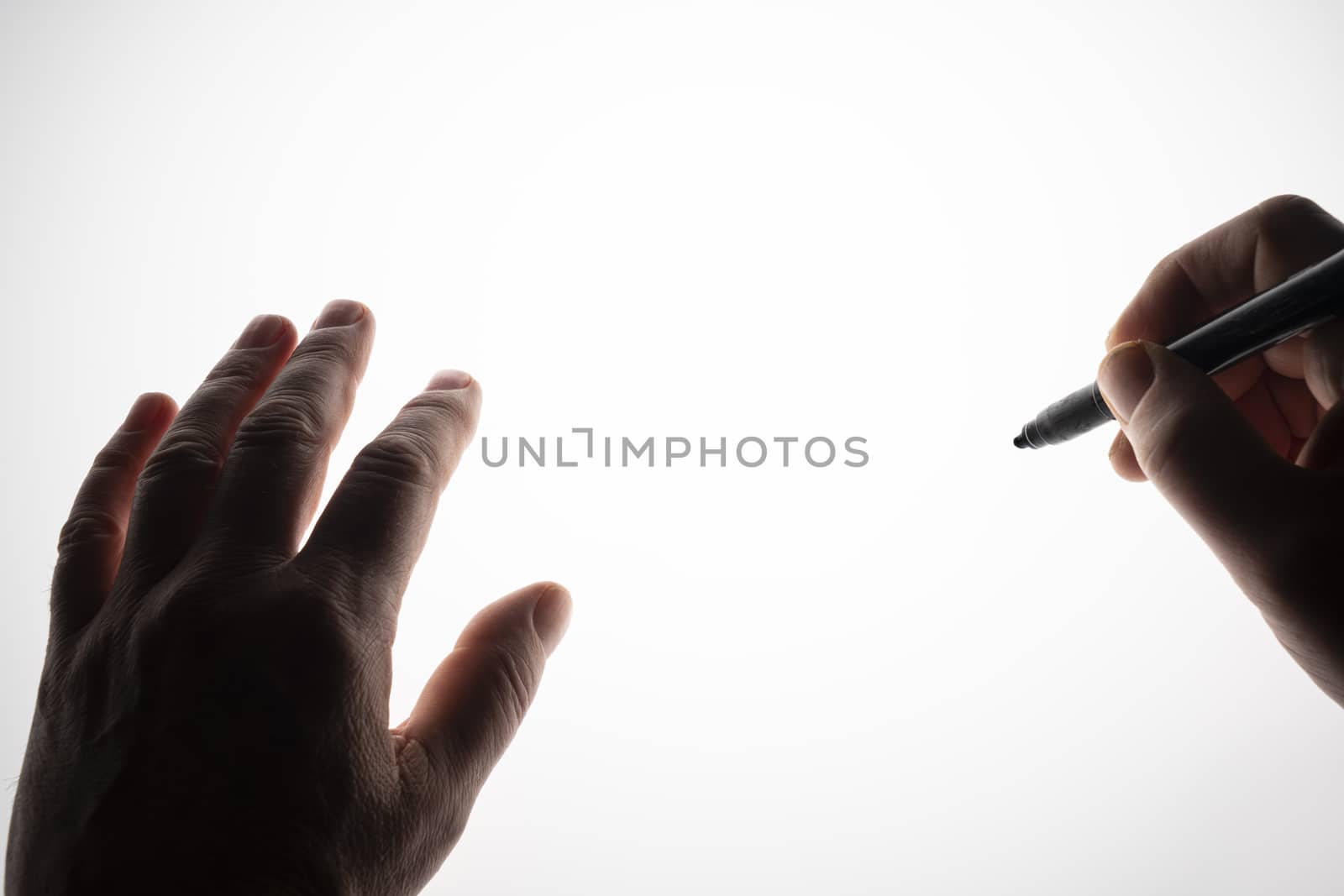 one hand writes with the pen on a backlit surface