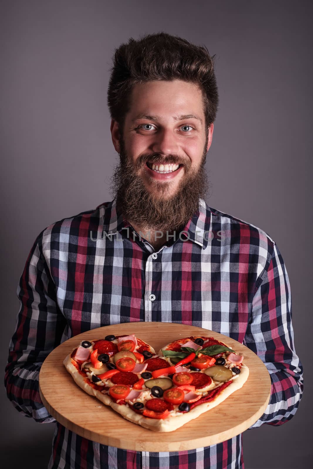 Happy smiling man holding home made heart shaped pizza for Valentines day