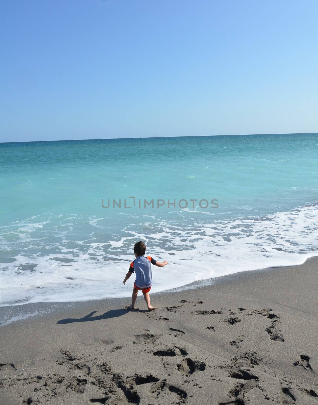 small boy child on the beach with footprints and ocean water