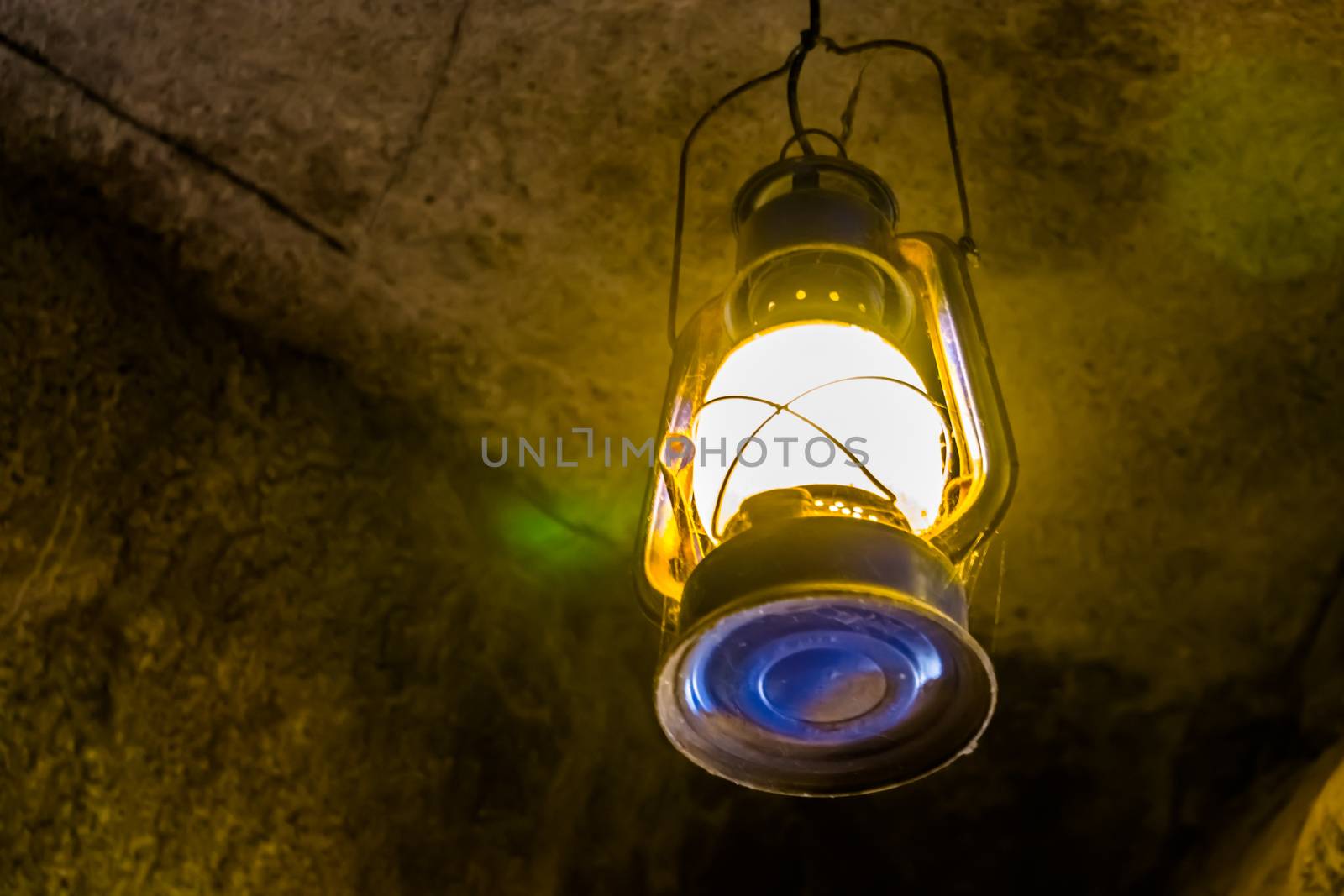 lighted vintage lantern hanging on the roof of a cave, nostalgic mining equipment