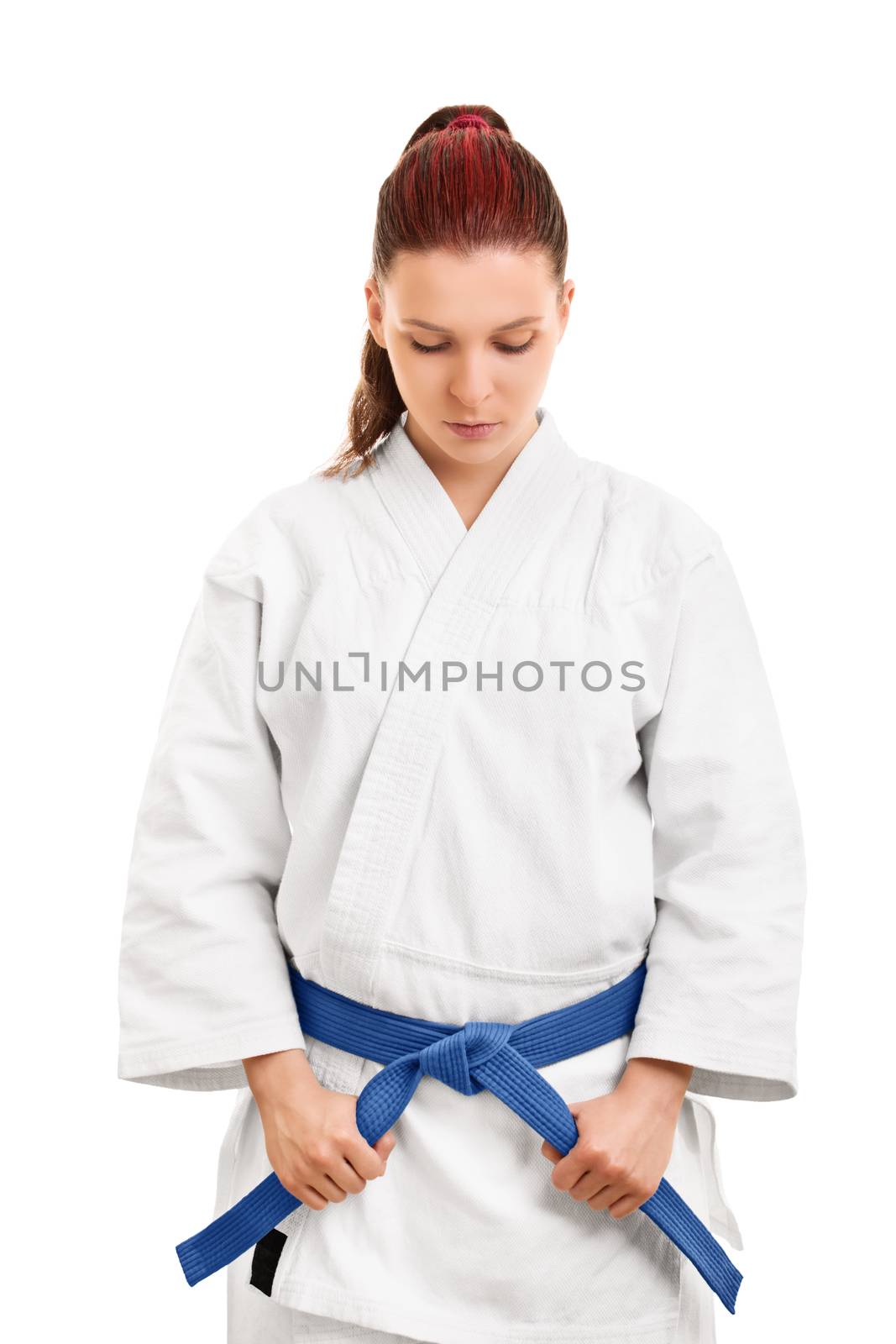 Portrait of a young female martial arts fighter in a white kimono holding her blue belt and looking down, isolated on white background. Concentrating before the fight. Giving respect concept.