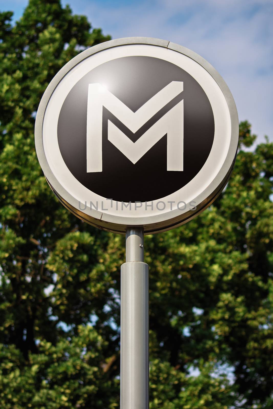 Transportation concept. Sign or symbol of Budapest city metro service located outdoor with trees and sky in the background. Metro sign with trees in the background.