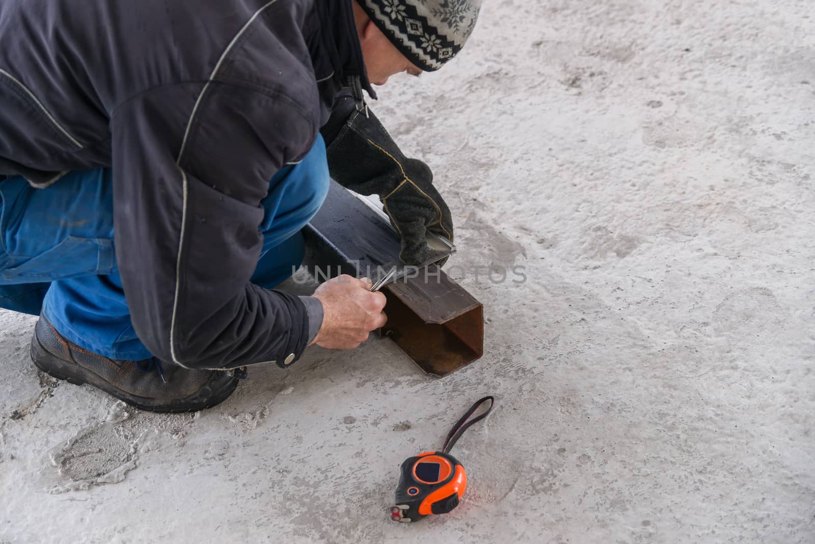 A builder draws on a square metal pipe using a locksmith on the concrete floor.