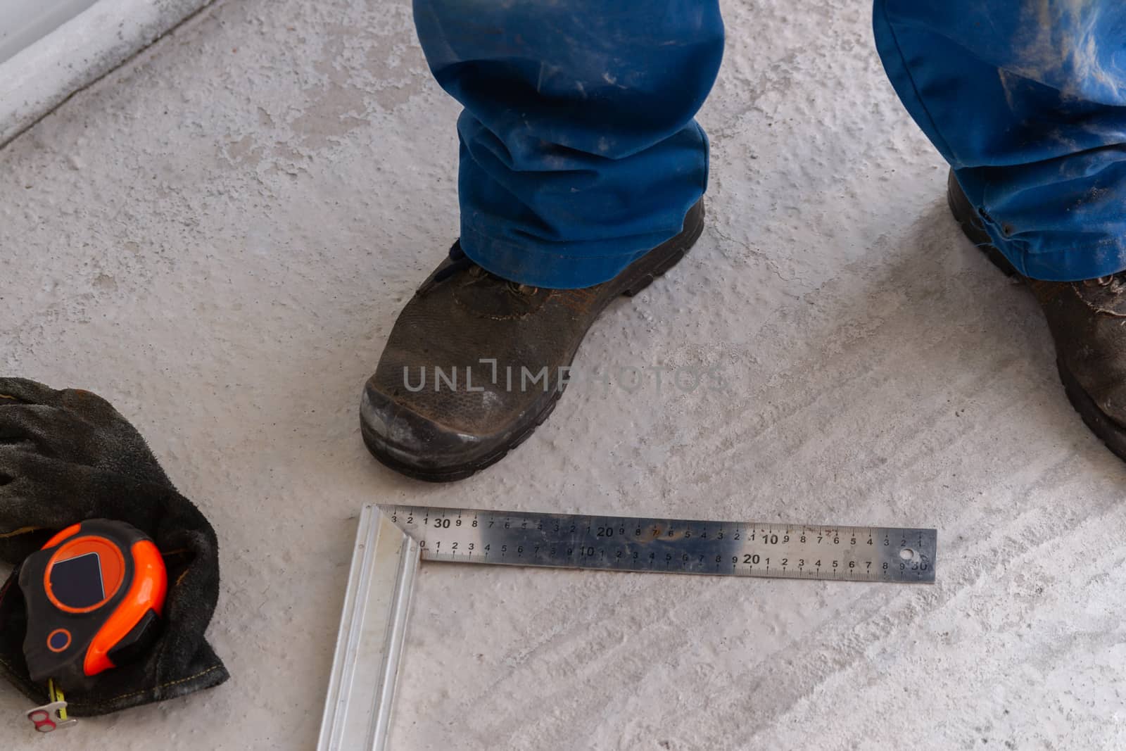 A man is standing on a concrete floor unfinished construction near ruler, measuring tape and metal setsquare.
