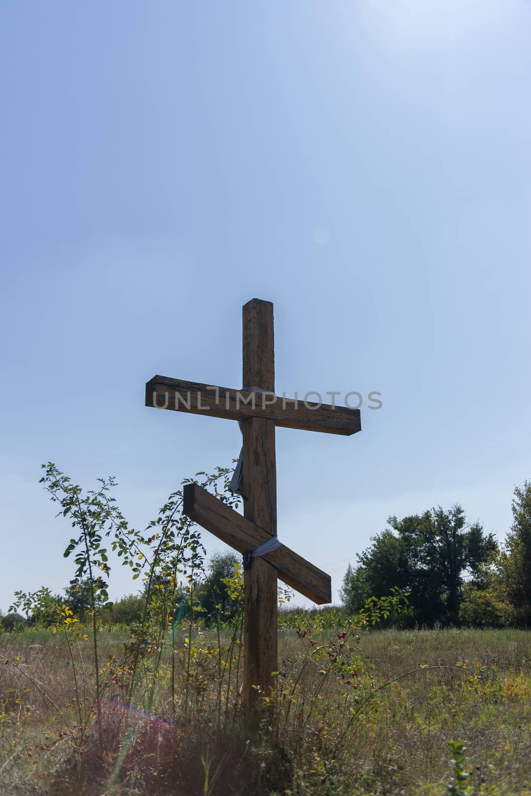 A wooden cross in the middle of the field. Christian symbol. by alexsdriver