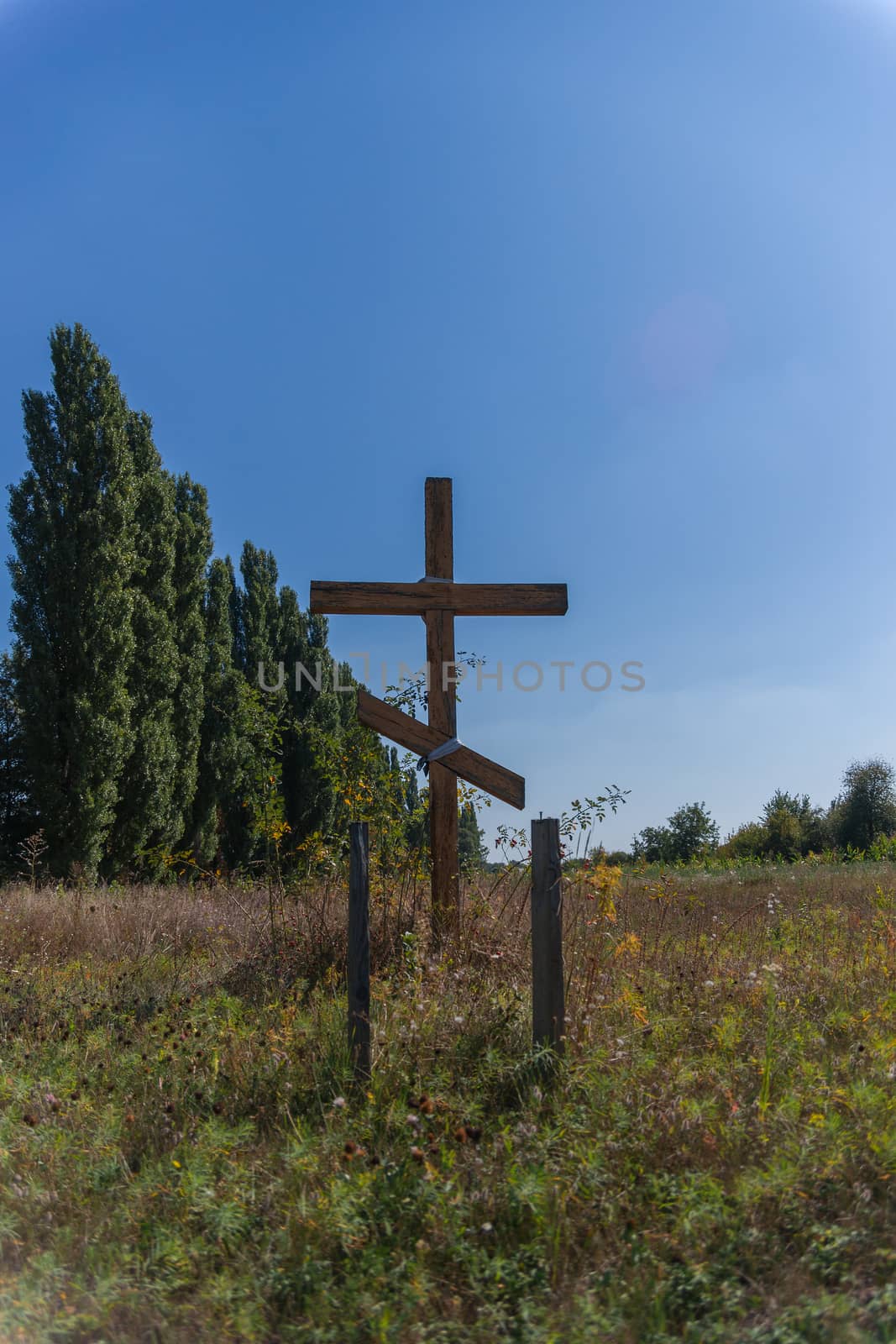 A wooden cross in the middle of the field. Christian symbol.