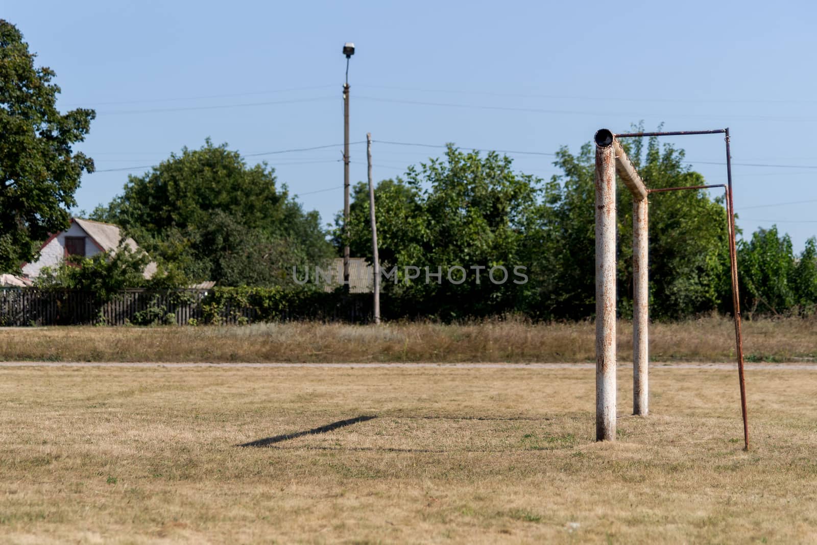 The empty football field with soccer goal in village. The grass is old and yellow.