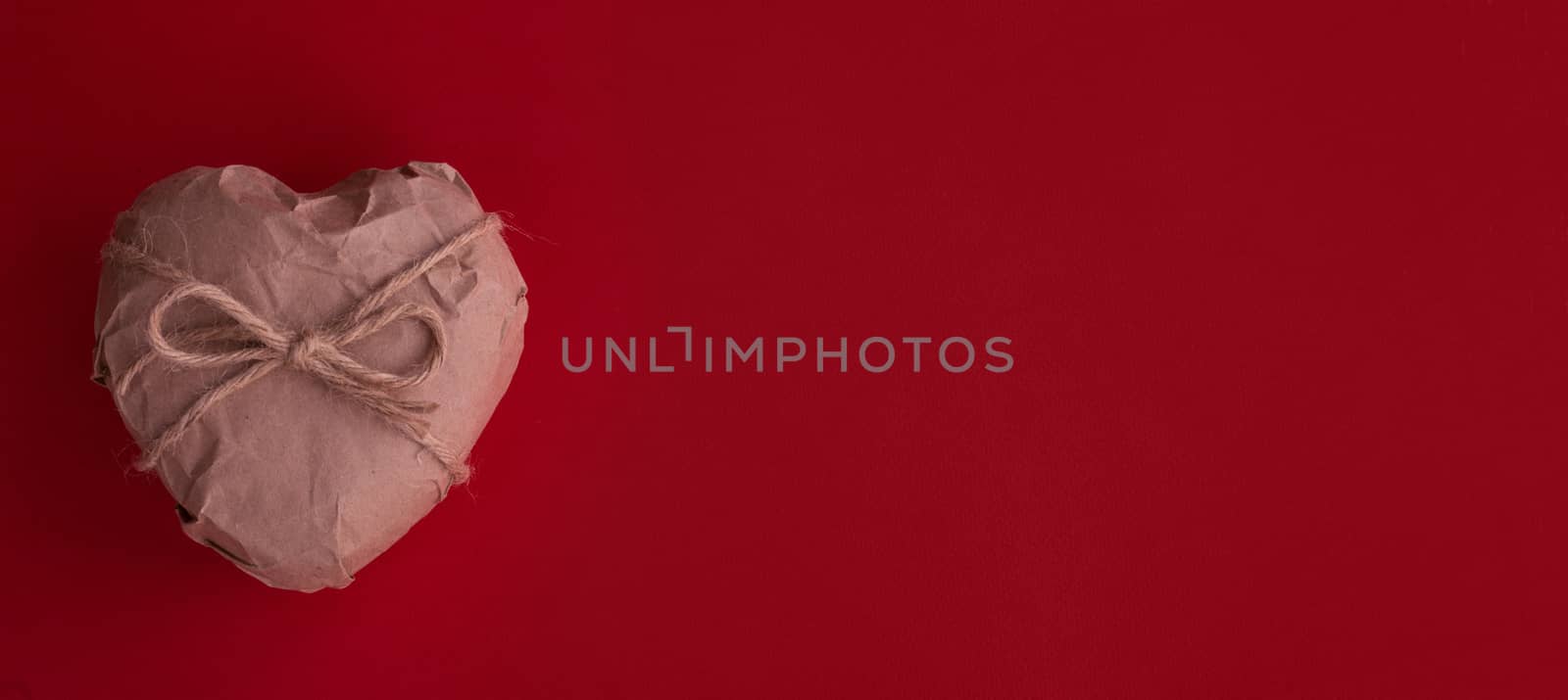 Heart in brown Wrapping Paper tied with rope bow on red background Valentine day surprise concept