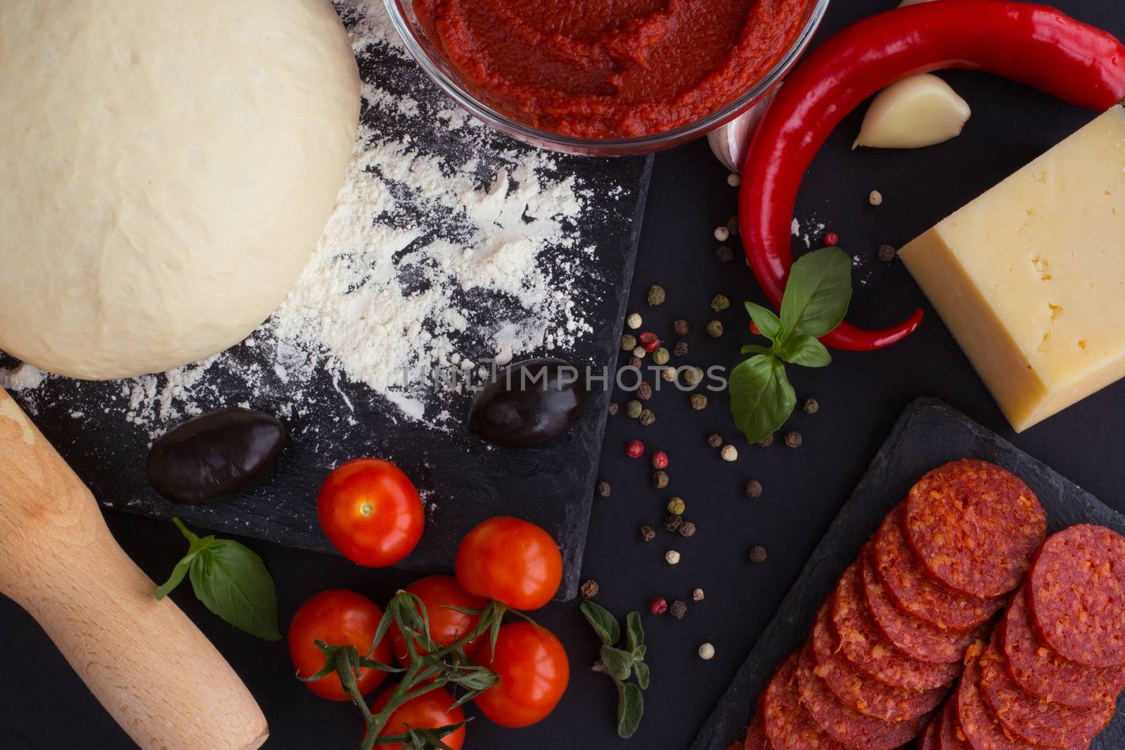 Raw dough for pizza with ingredients and spices on black table background