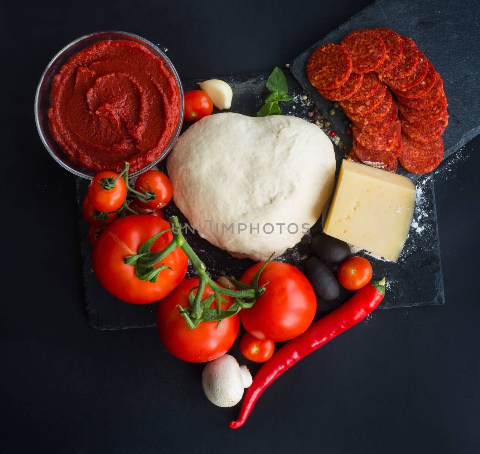 Raw dough for pizza with ingredients and spices on black table background in heart shape love food of Valentines day concept