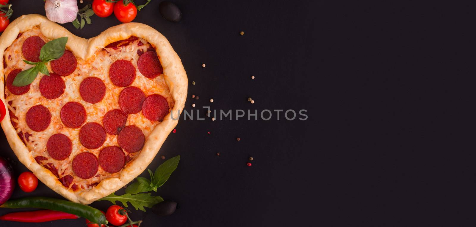 Pizza heart shaped with pepperoni with ingredients on black background. Concept of romantic love for Valentines Day . Love food