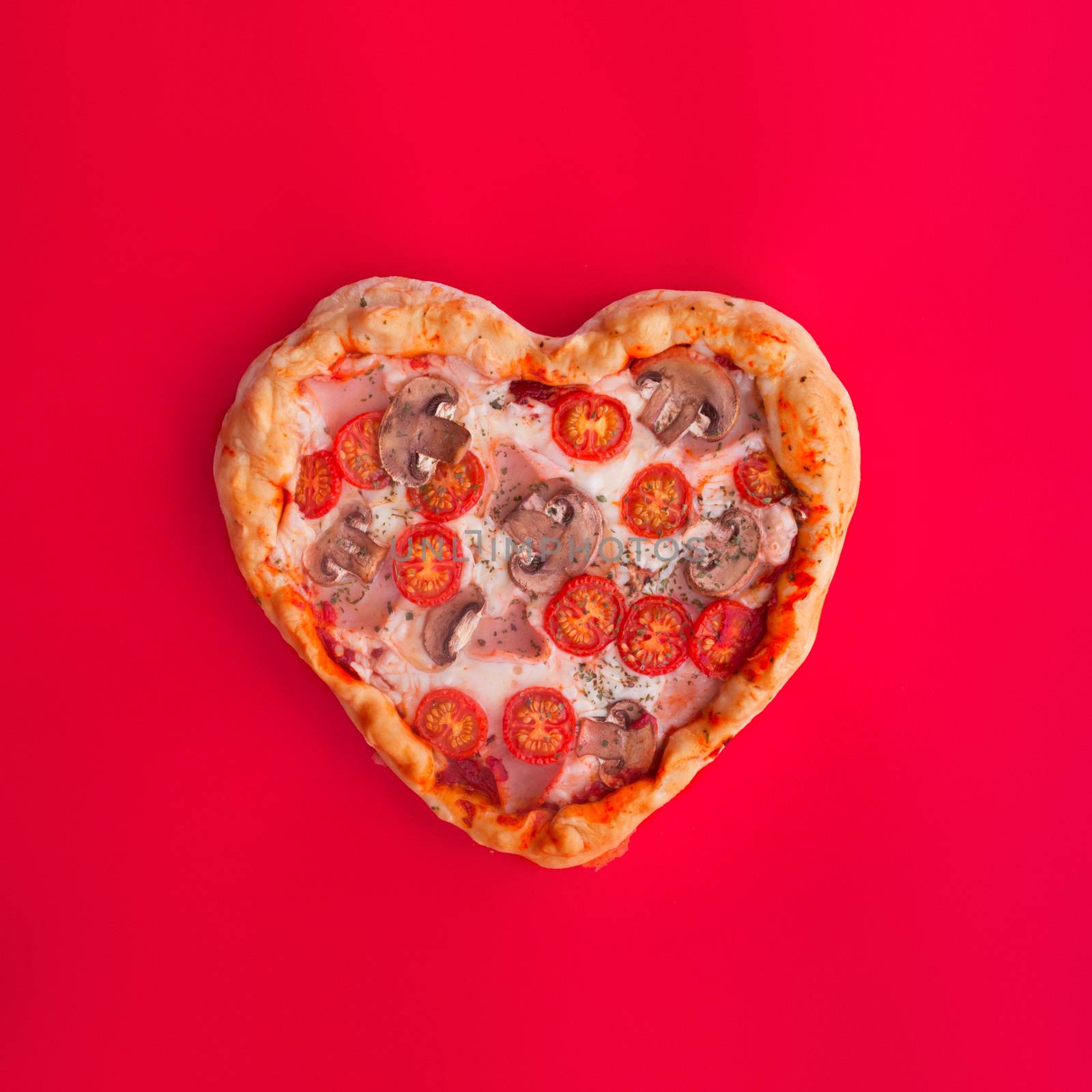Pizza heart shaped with ham tomatoes and mushrooms on red background. Concept of romantic love for Valentines Day . Love food