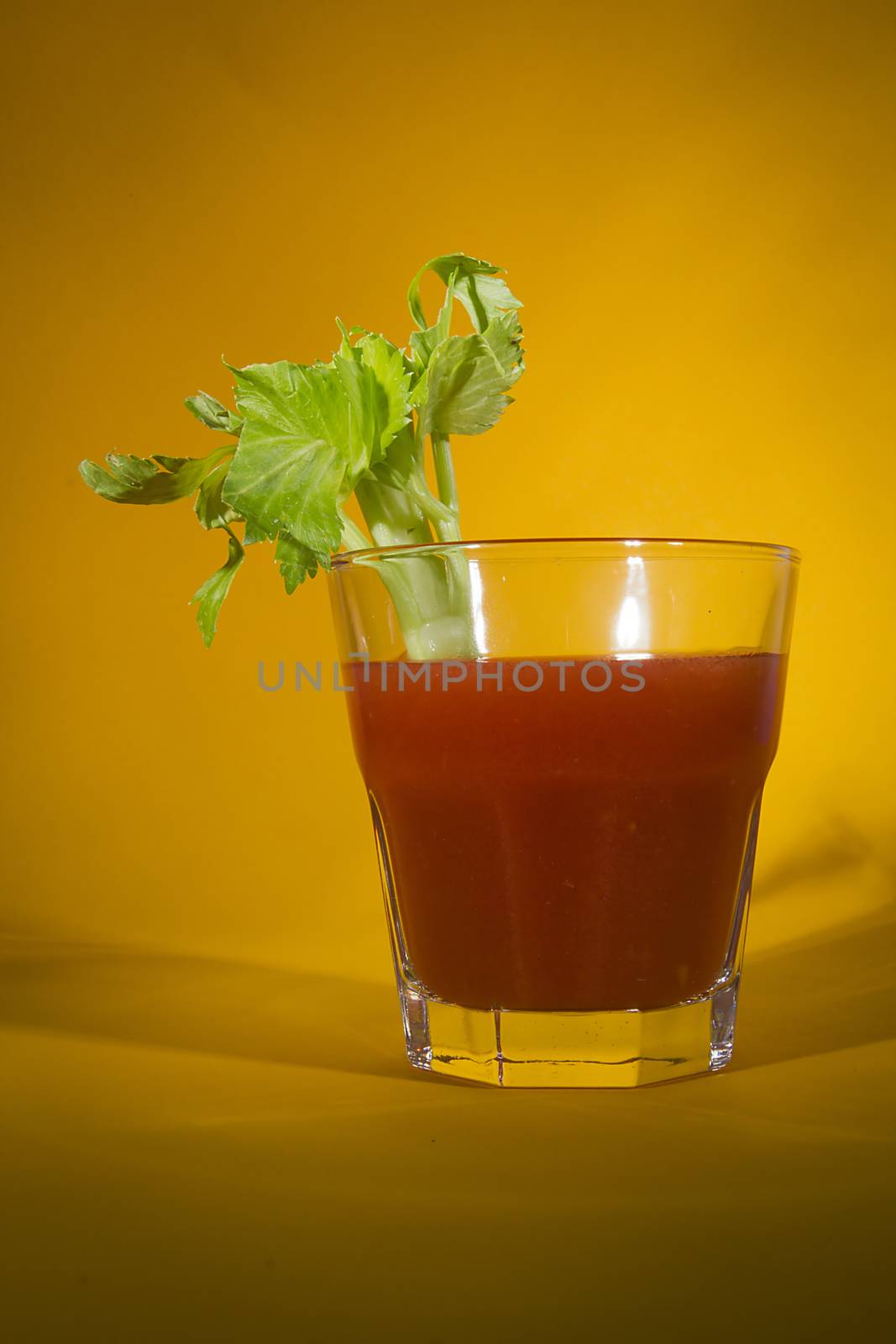 Bloody Mary cocktail with a branch of celery on a yellow background
