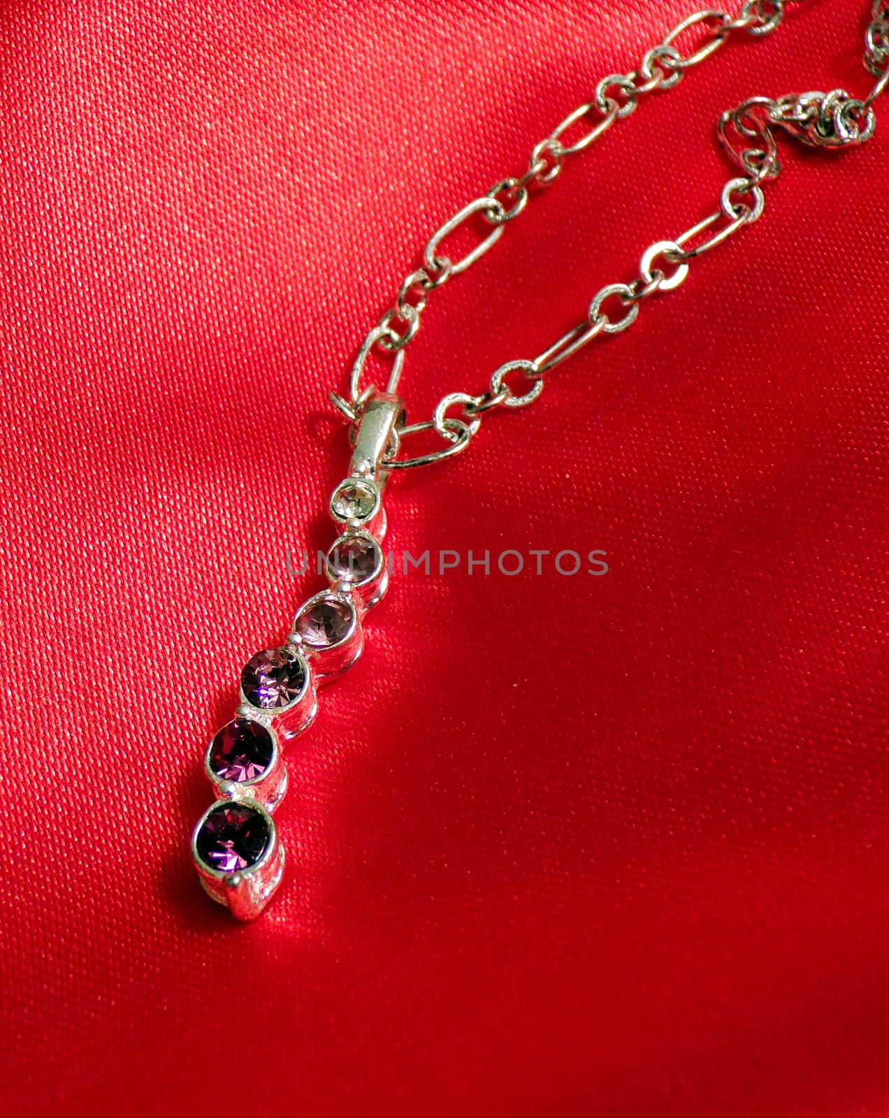 Jewelry pendant with precious stones and a chain on a silk red fabric.