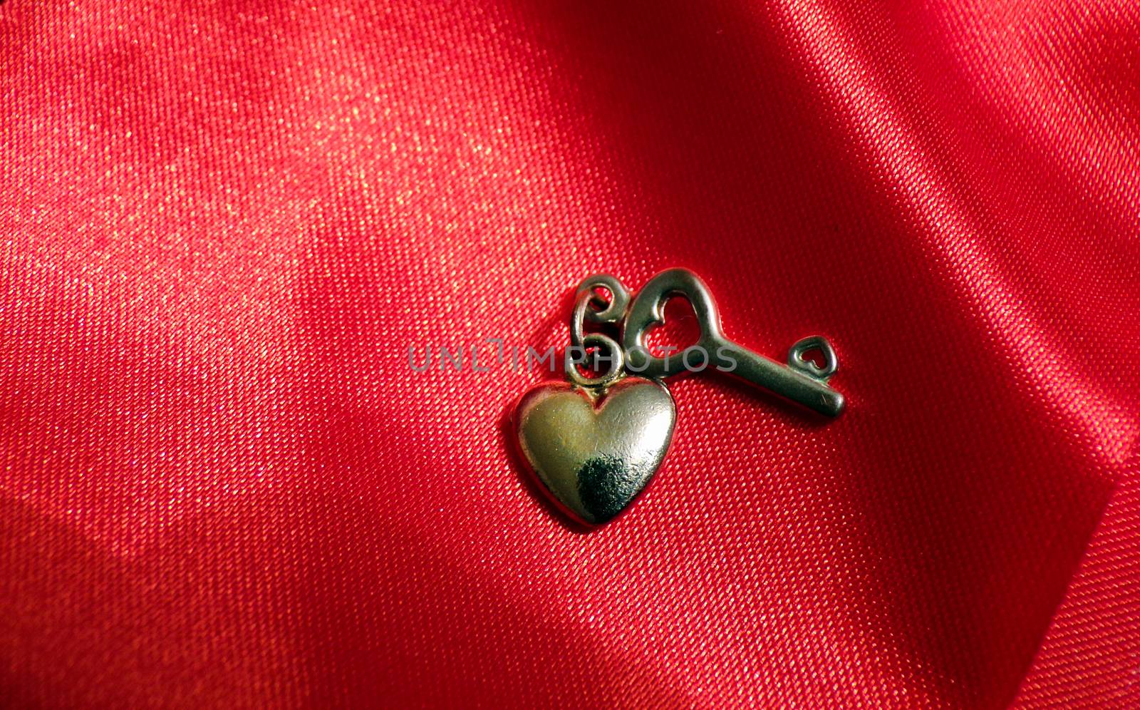 Romantic love background for Valentine's day. Heart and key made of metal on a red silk fabric.