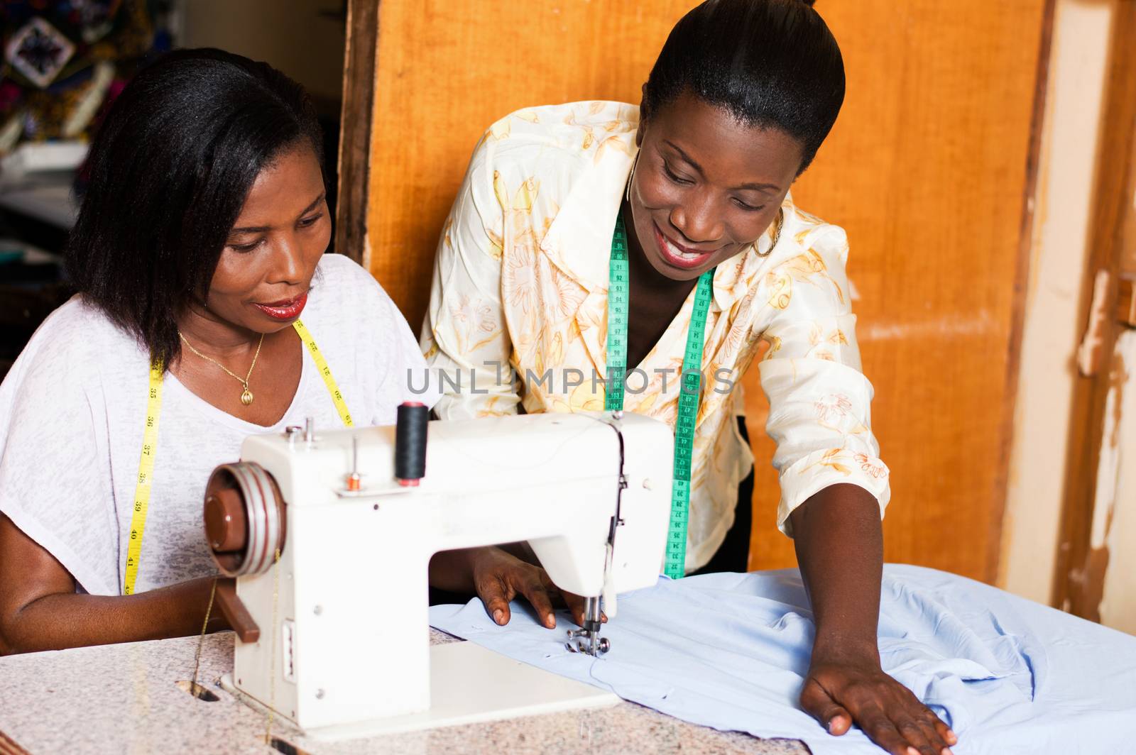 seamstress teaches her  students how to put a shirt under the needle of a sewing machine.