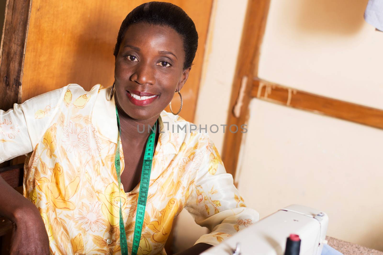 Beautiful woman seamstress smiling sitting behind a sewing machine with her tape measure at the neck.