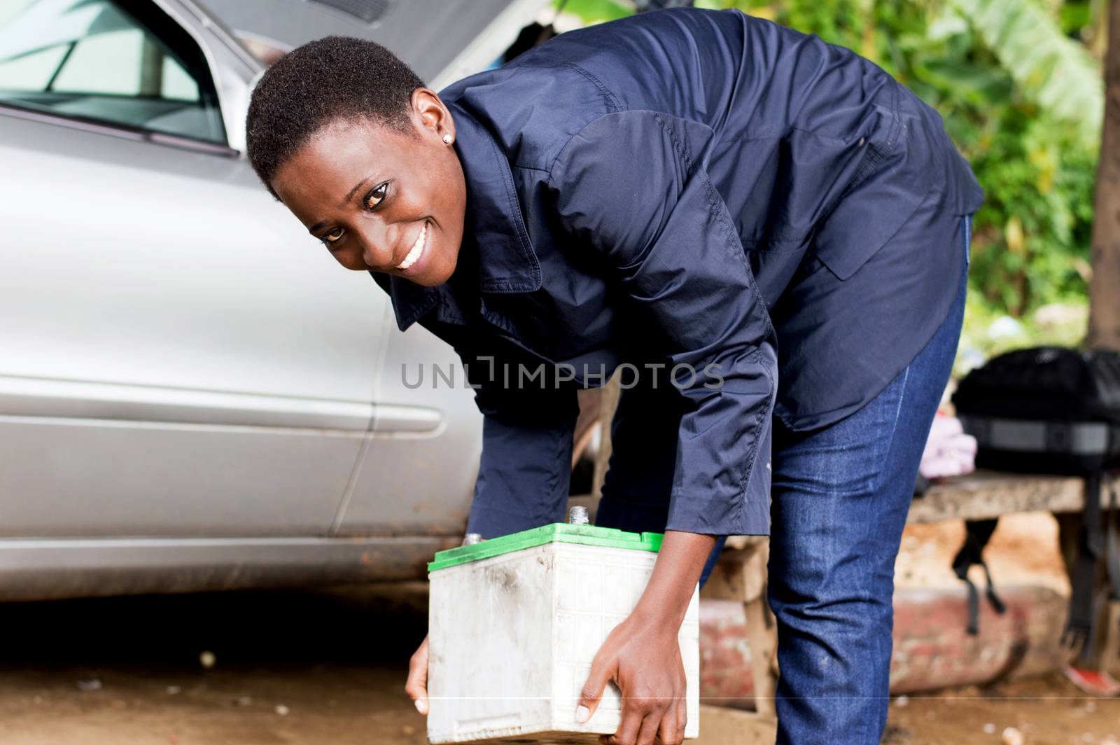 Young woman mechanic lifting a car battery in her workshop.