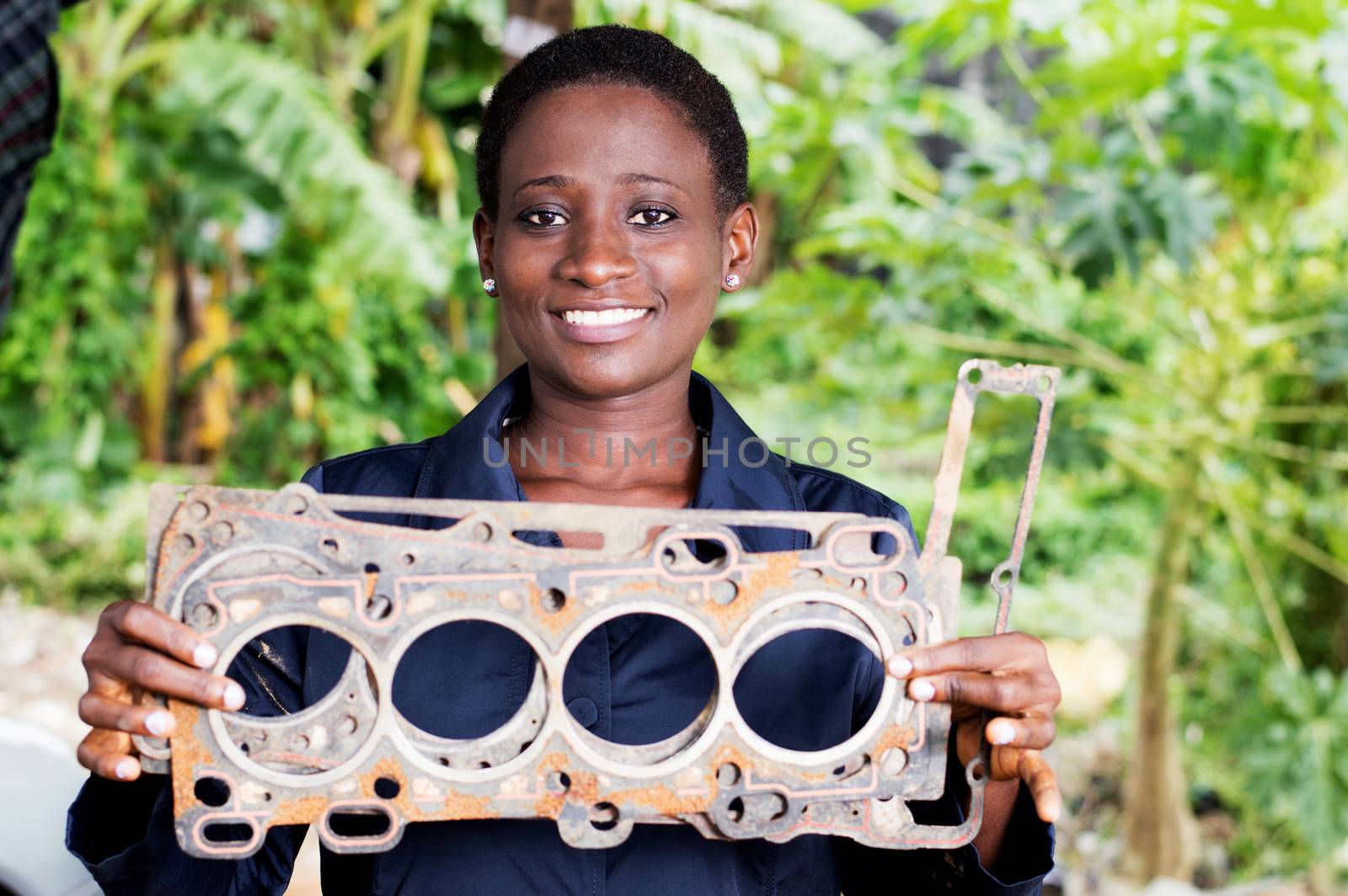 Young woman mechanic holds a damaged car part in her workshop.