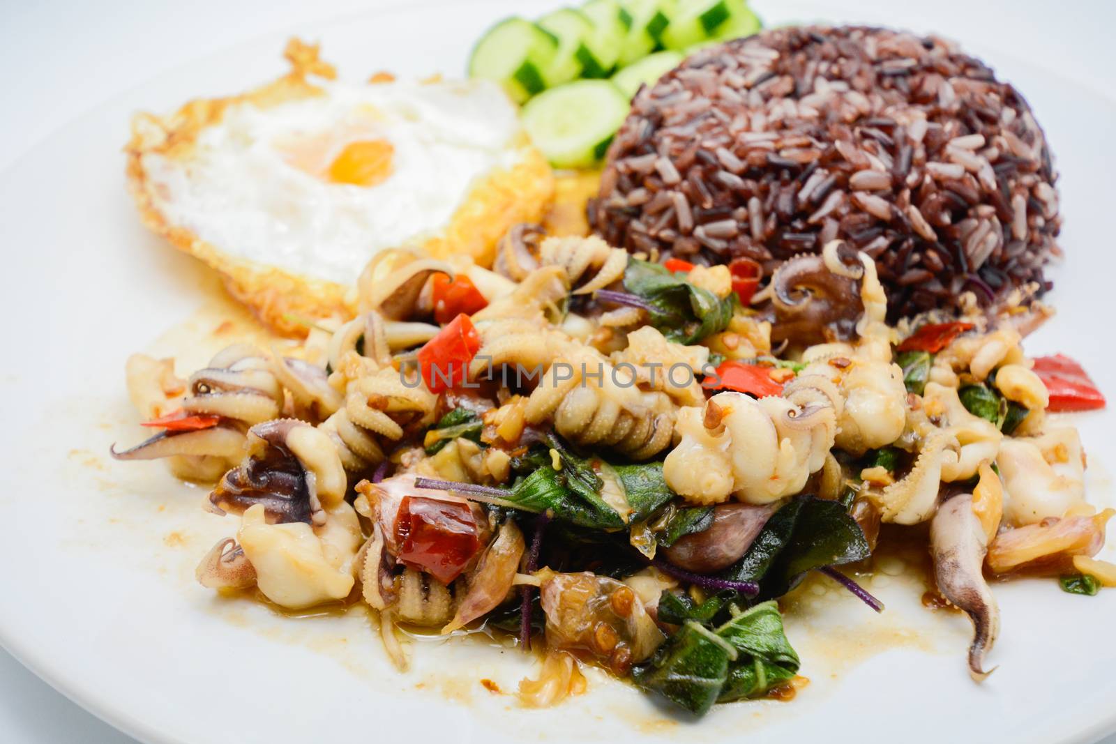 Spicy stir fried squid with basil leaves and chili, Sunny side up egg, served with brown rice. It is famous Thai food. You can change material designed and try to cook for your family.