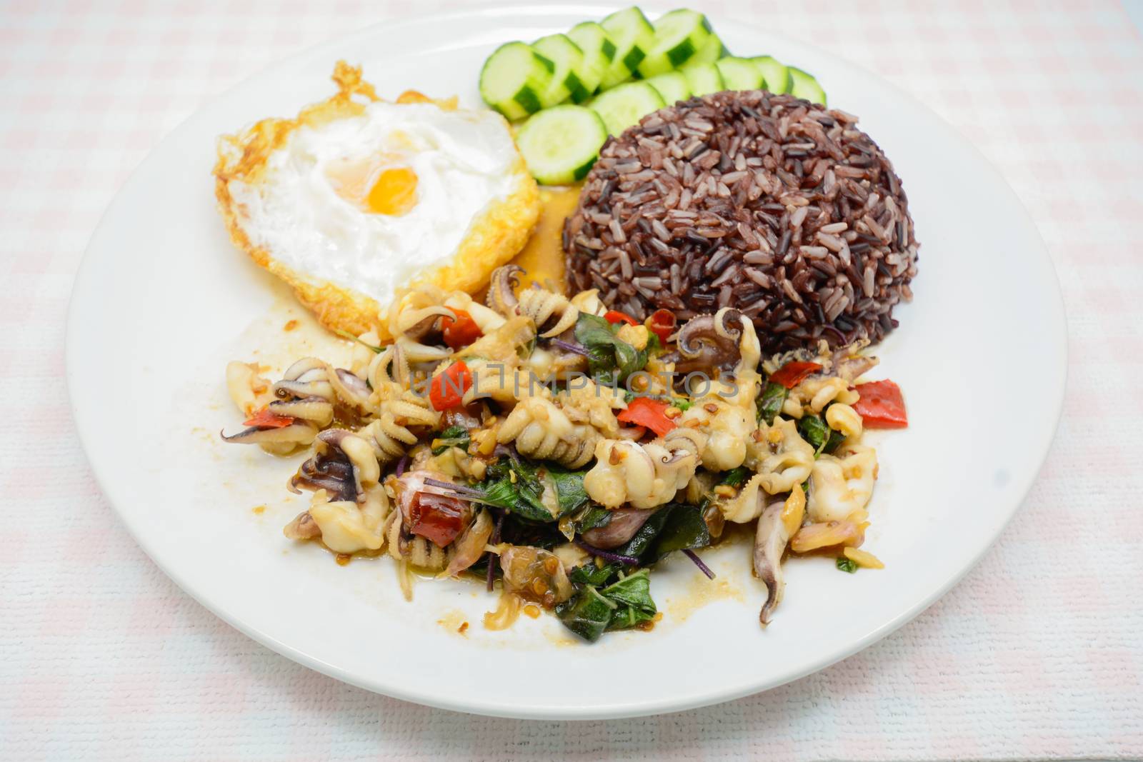 Spicy stir fried squid with basil leaves and chili, Sunny side up egg, served with brown rice. It is famous Thai food. You can change material designed and try to cook for your family.