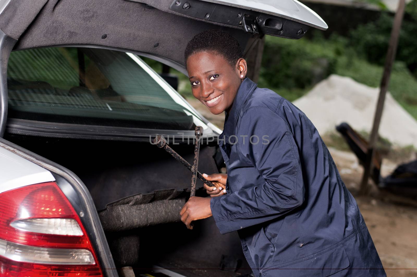 Young smiling mechanic takes her tool from the back of a car in the garage.
