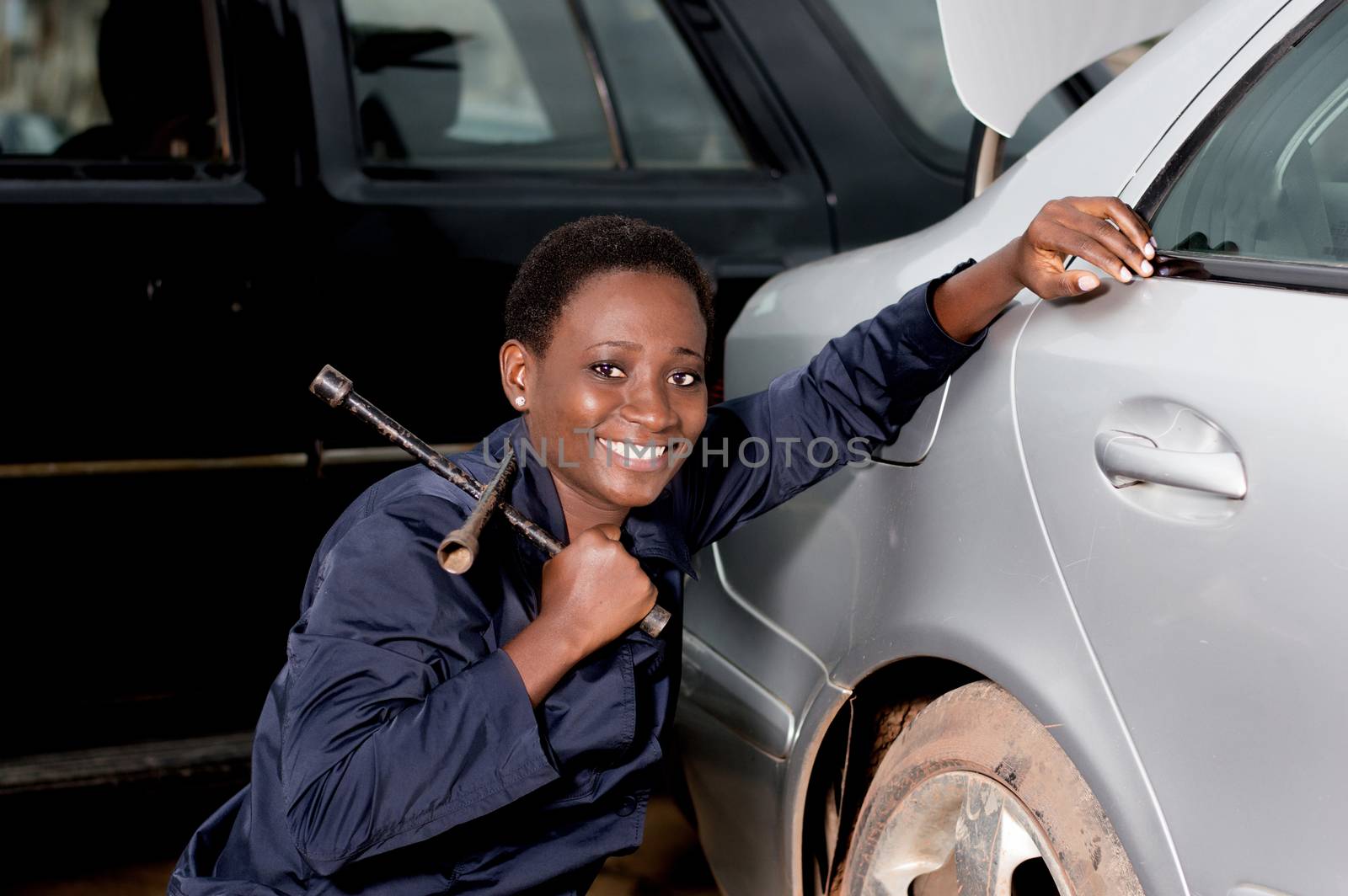 Young smiling mechanic squatting near the tire of a car she is preparing to remove.