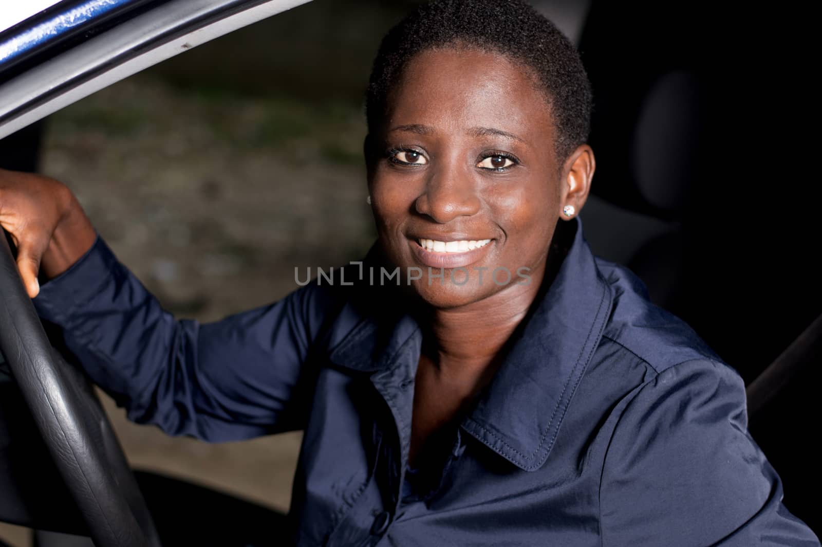 Young woman sitting in a car, hands on the steering wheel smiling at the camera.
