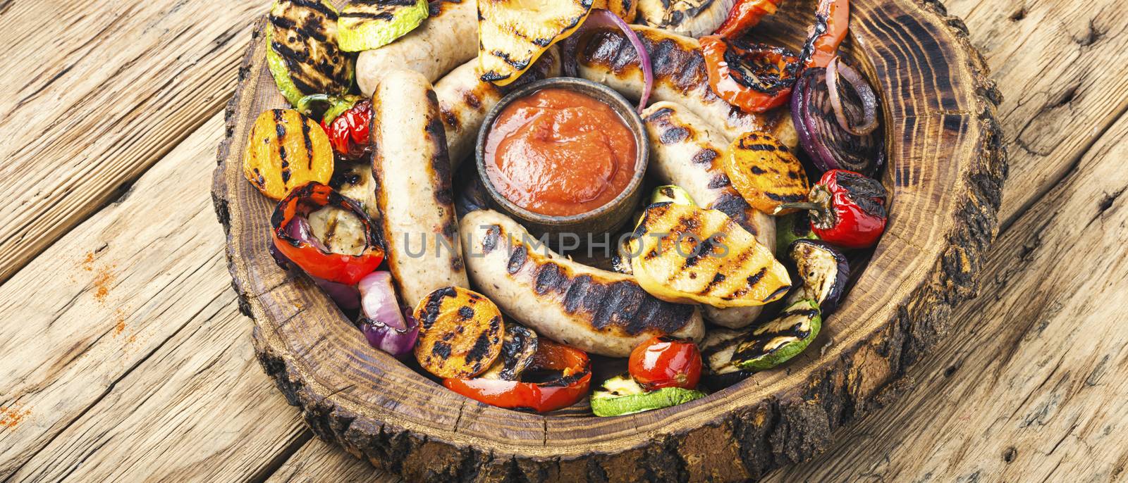 Grilled sausages and vegetables with sauce ketchup on wooden tray.Bbq food