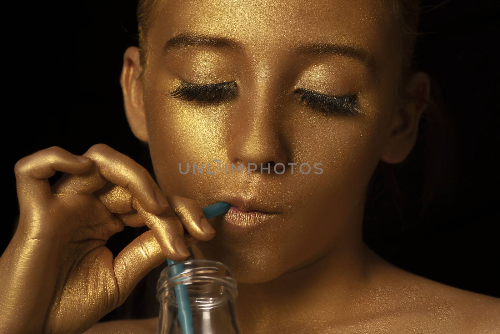 Beauty woman face makeup close up.Gold Fashion Model Beauty Portrait with a bottle and a cocktail straw , Golden Woman Art Makeup on studio black background.