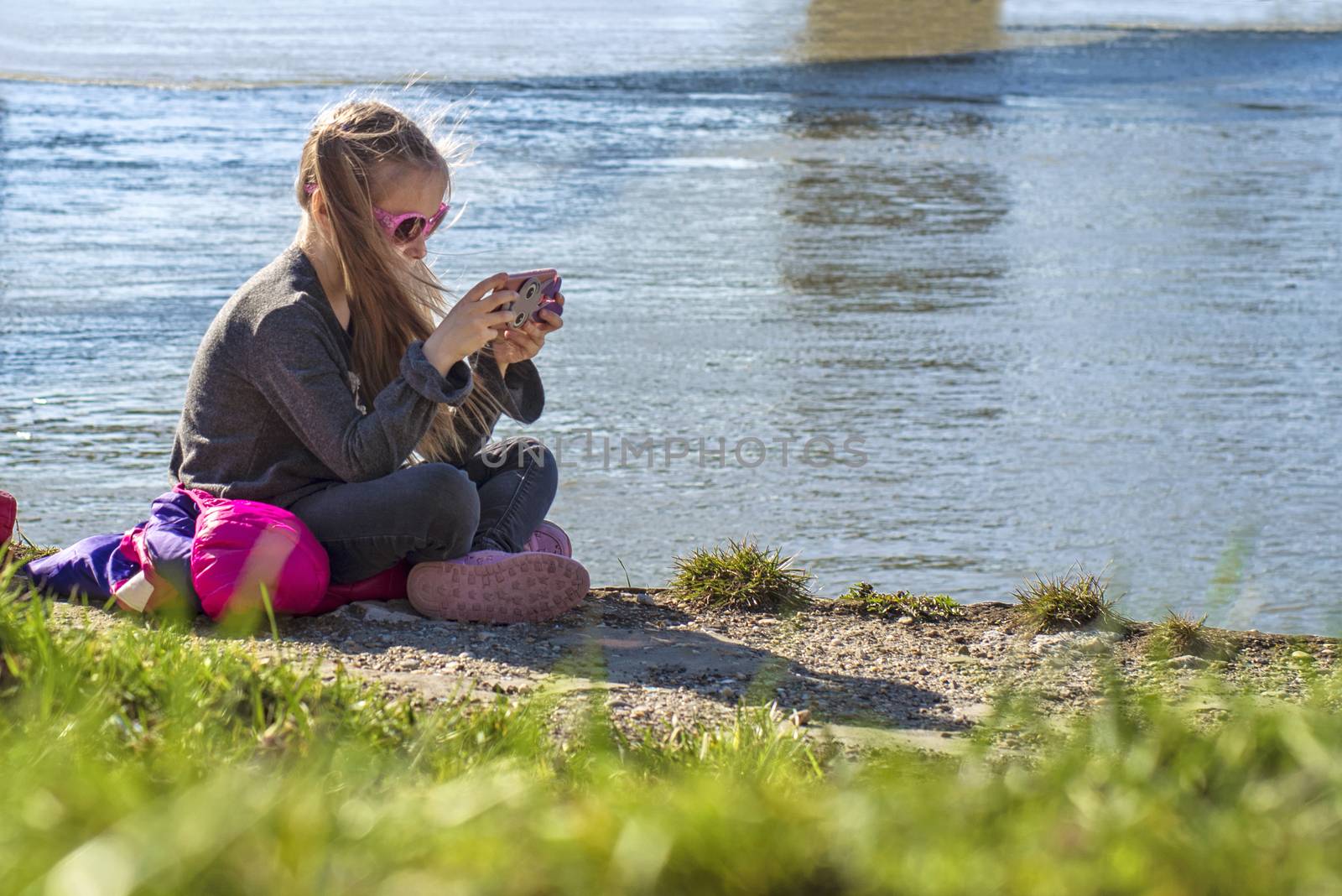 A little girl is sitting on the bank of the river with a telephone. On a warm spring day. by nkooume
