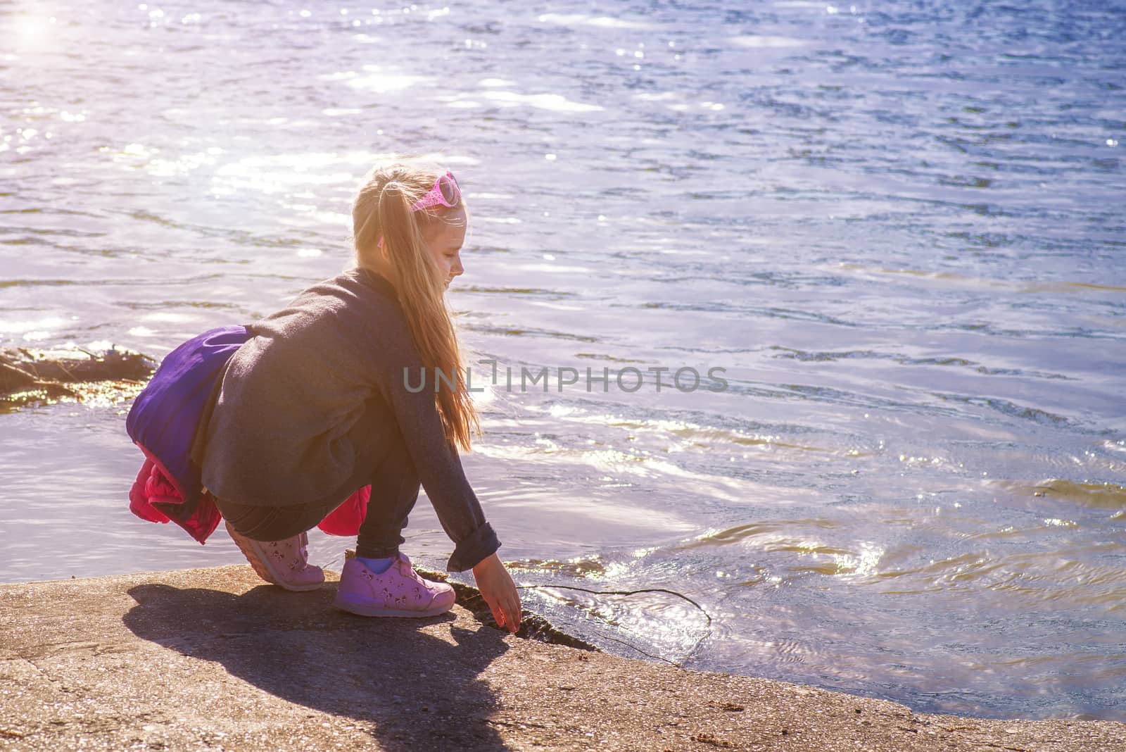 Little girl by the river.Little girl sitting alone and thinking about something on the pier. Selective focus on the girl.