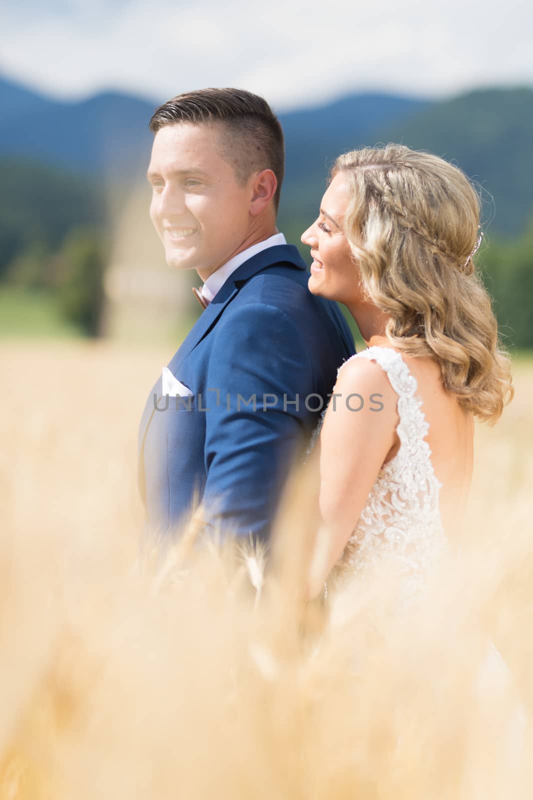 Newlyweds hugging tenderly in wheat field somewhere in Slovenian countryside. Caucasian happy romantic young couple celebrating their marriage.