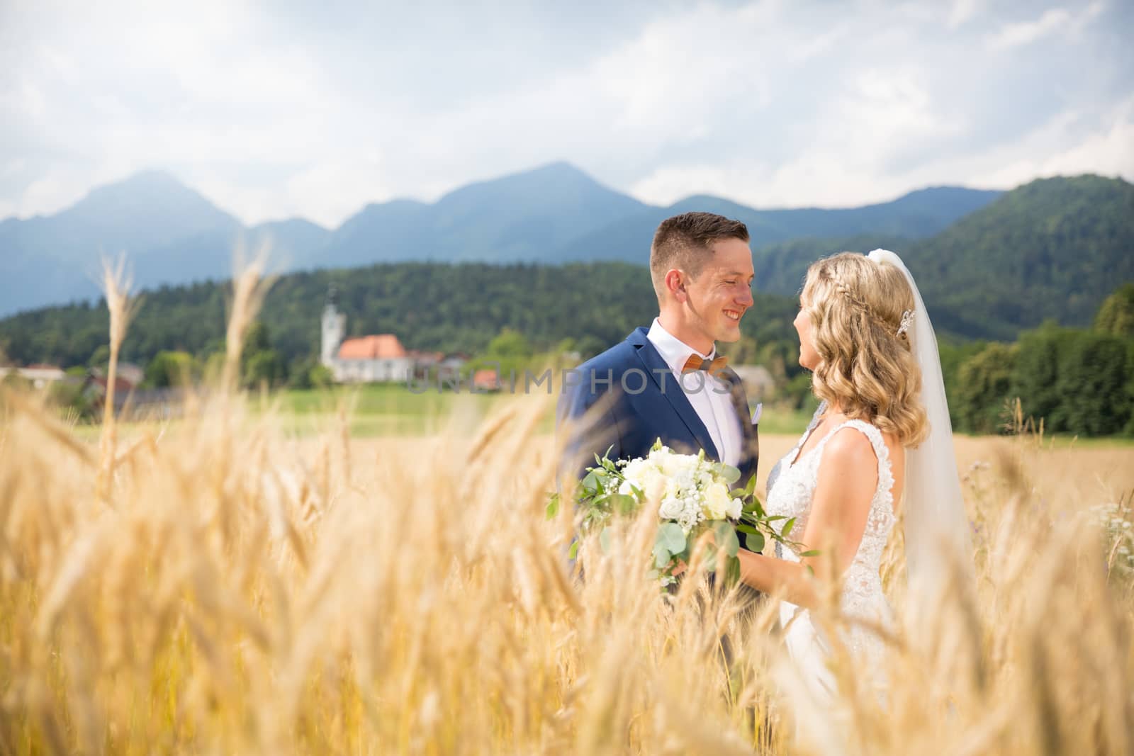 Groom hugs bride tenderly in wheat field somewhere in Slovenian countryside. Caucasian happy romantic young couple celebrating their marriage.
