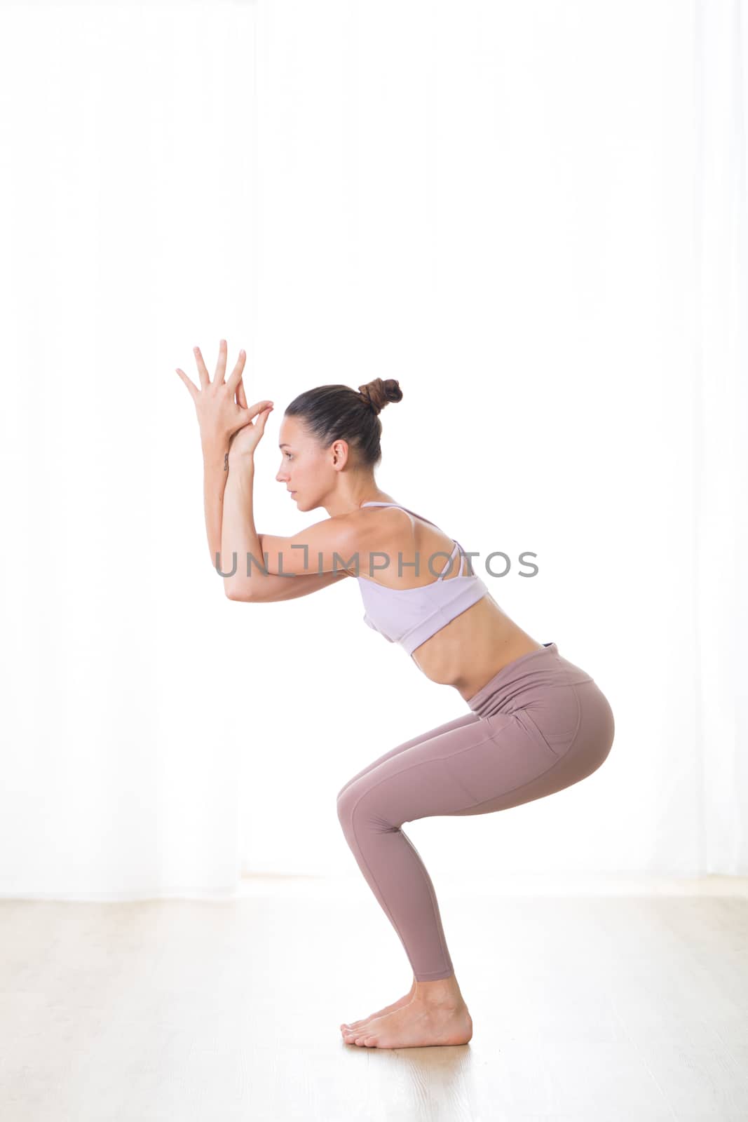 Portrait of gorgeous active sporty young woman practicing yoga in studio. Beautiful girl practice Garurasana, eagle yoga pose. Healthy active lifestyle, working out indoors in gym by kasto