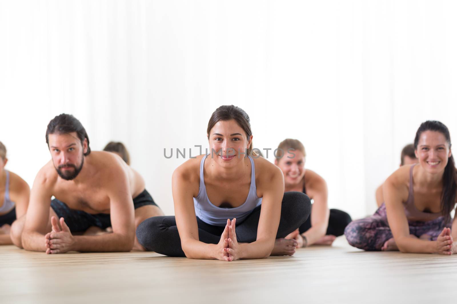 Group of young sporty attractive people in yoga studio, practicing yoga lesson with instructor, sitting on floor in forward band stretching yoga pose. Healthy active lifestyle, working out in gym by kasto