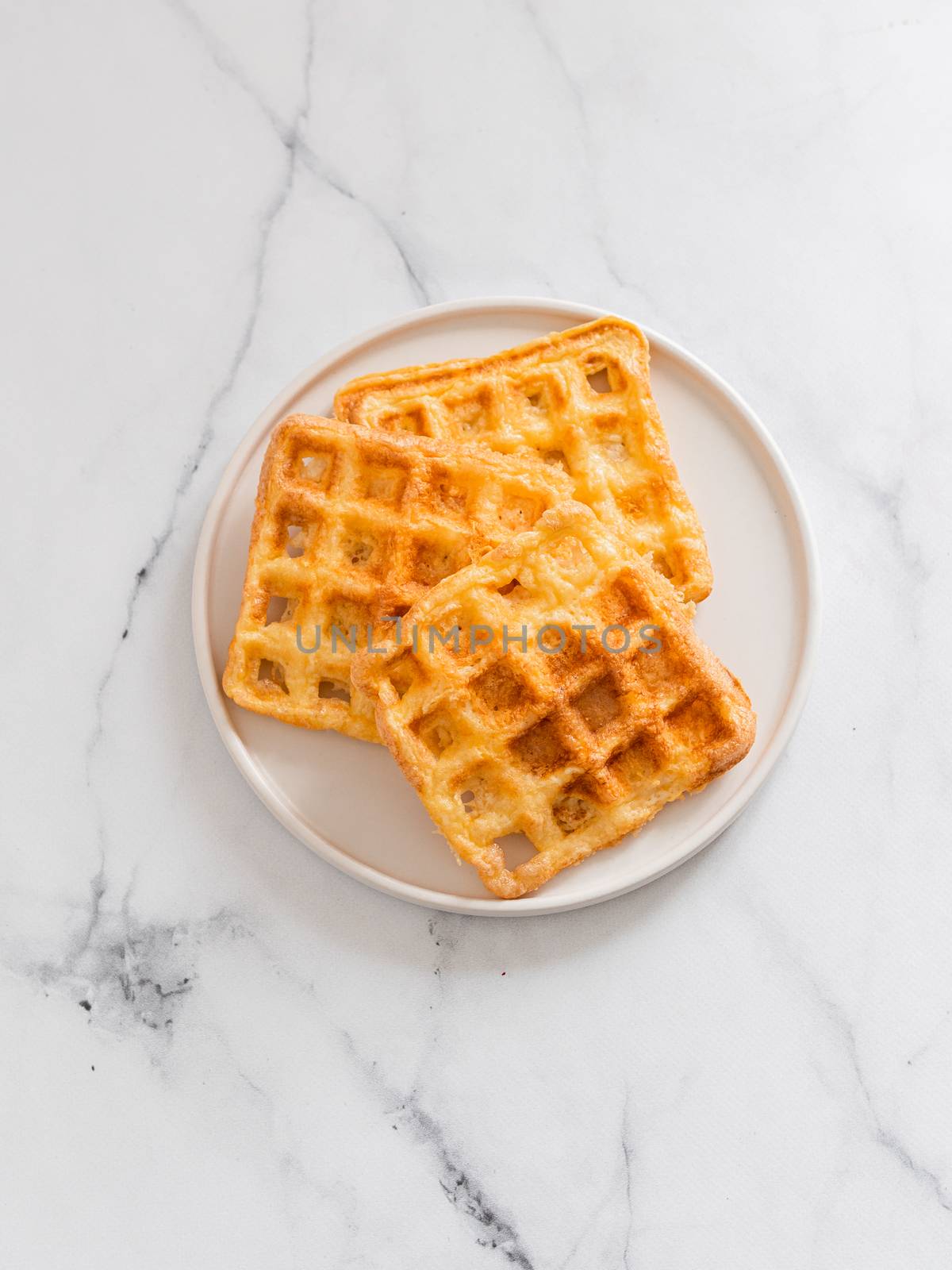 Perfect savory keto waffles. Two ingredients chaffles on plate over white marble background. Eggs and parmesan cheese low carb waffles. Top view or flat lay. Copy space for text or design. Vertical.