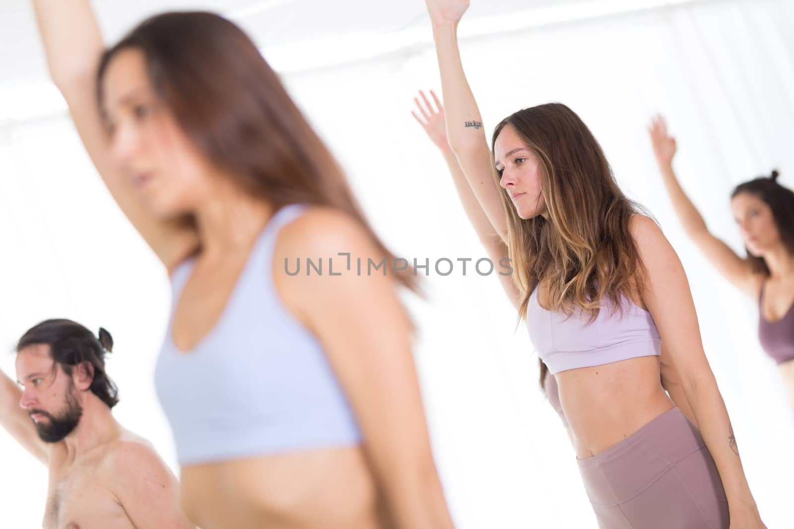 Group of young sporty attractive women in yoga studio, practicing yoga lesson with instructor, standing, stretching and relaxing after workout . Healthy active lifestyle, working out indoors in gym.