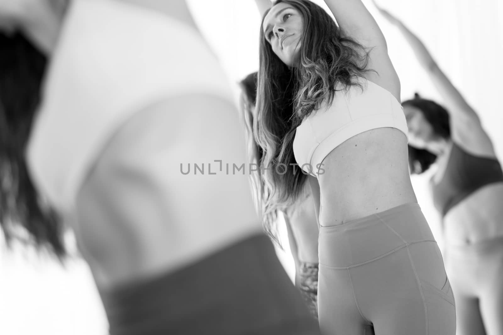 Group of young sporty attractive women in yoga studio, practicing yoga lesson with instructor, standing, stretching and relaxing after workout . Healthy active lifestyle, working out. Black and white.