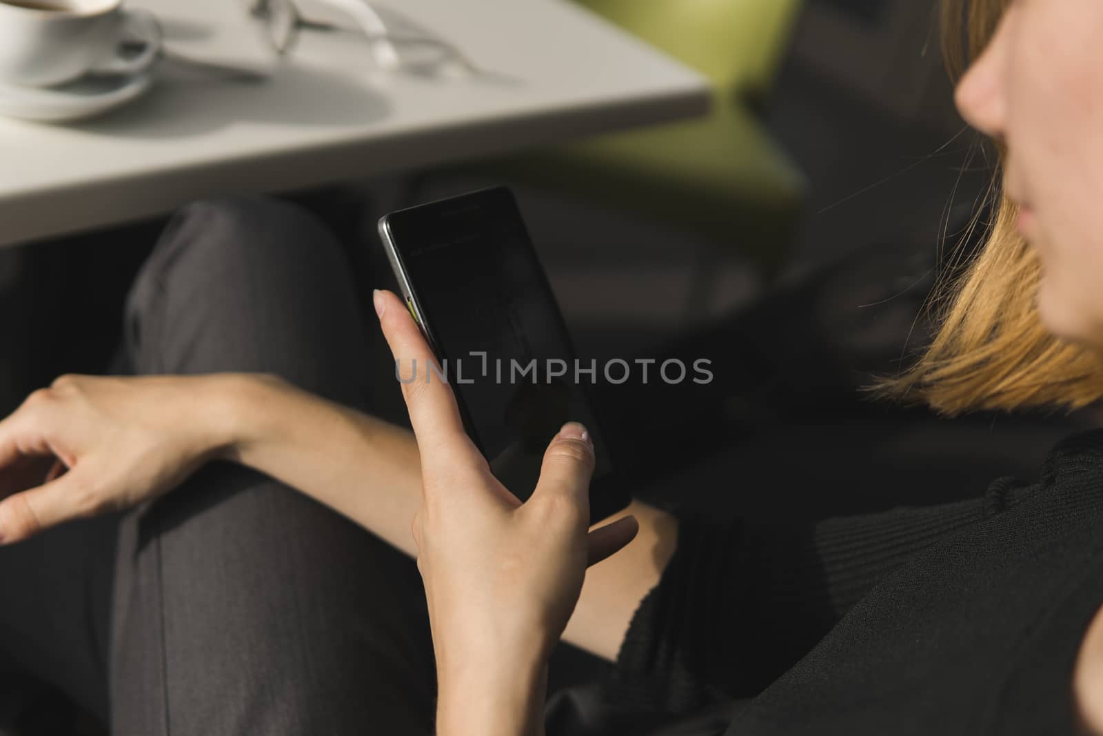 Young business woman uses phone. Good looking brunette female uses online banking on smart phone to transfer money from credit card. Girl using smart phone and chatting with business partners