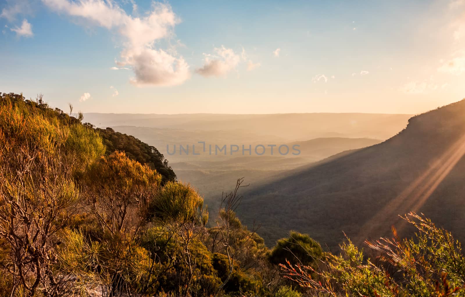 Views from the mountain escarpment into the valley in late afternoon, the sun's golden light streaming  across the landscape highlighting one side creating light and shadow