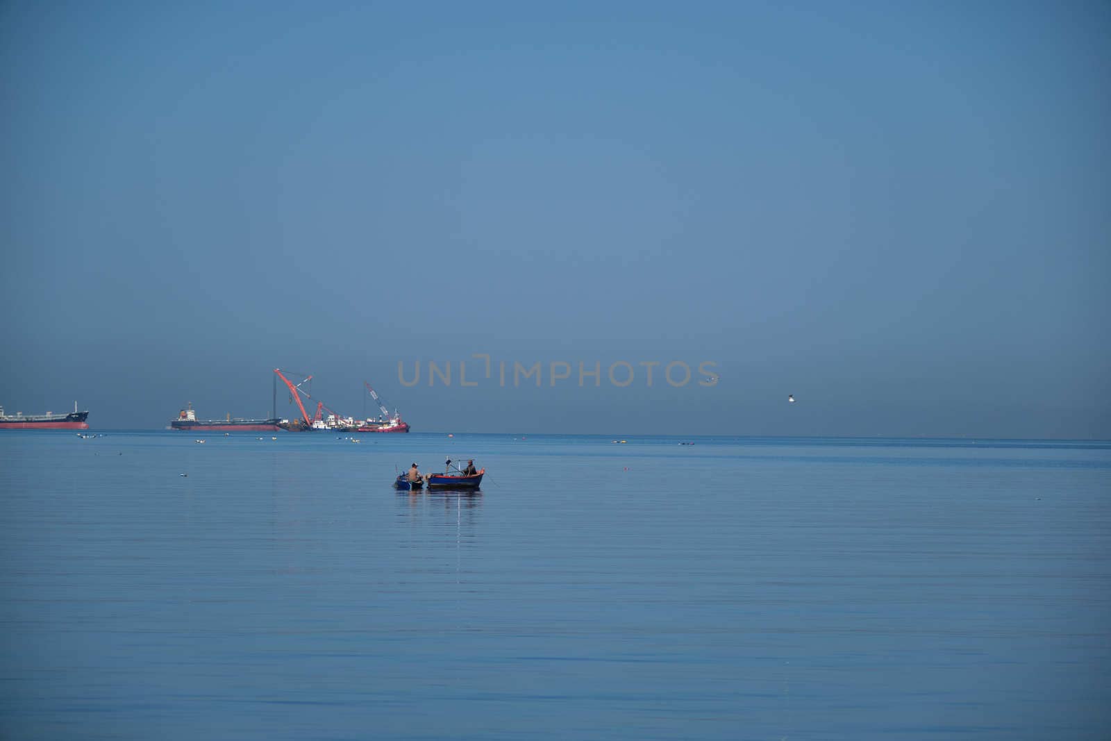 The Small Fisherman Boat in the Sea. A small fisherman boat floating on the sea near the seashore with Cargo ship background